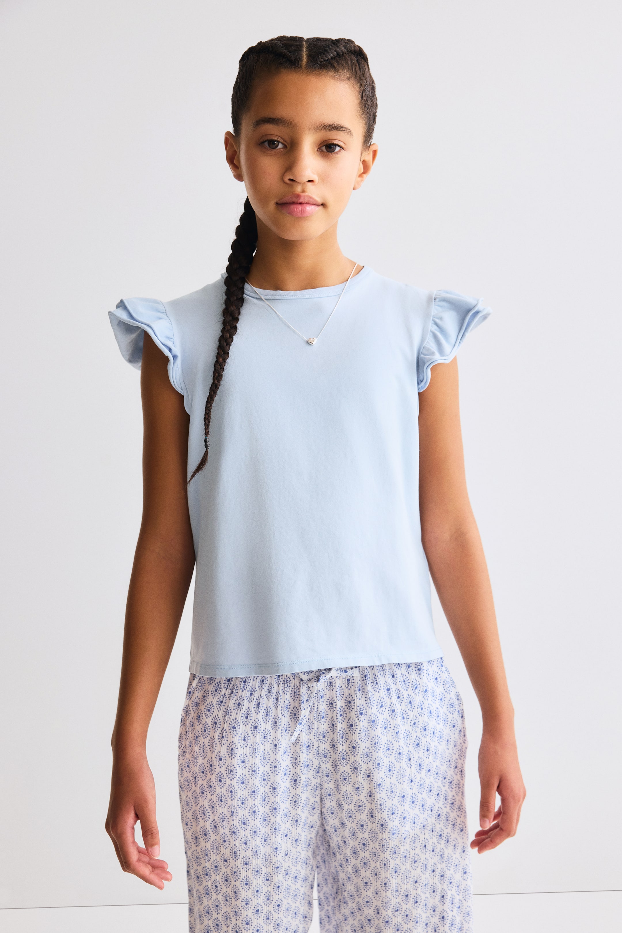 View larger image: A light blue top in soft cotton jersey featuring a round, rib-trimmed neckline and double-layered flutter sleeves with roll edges, shown from the front.