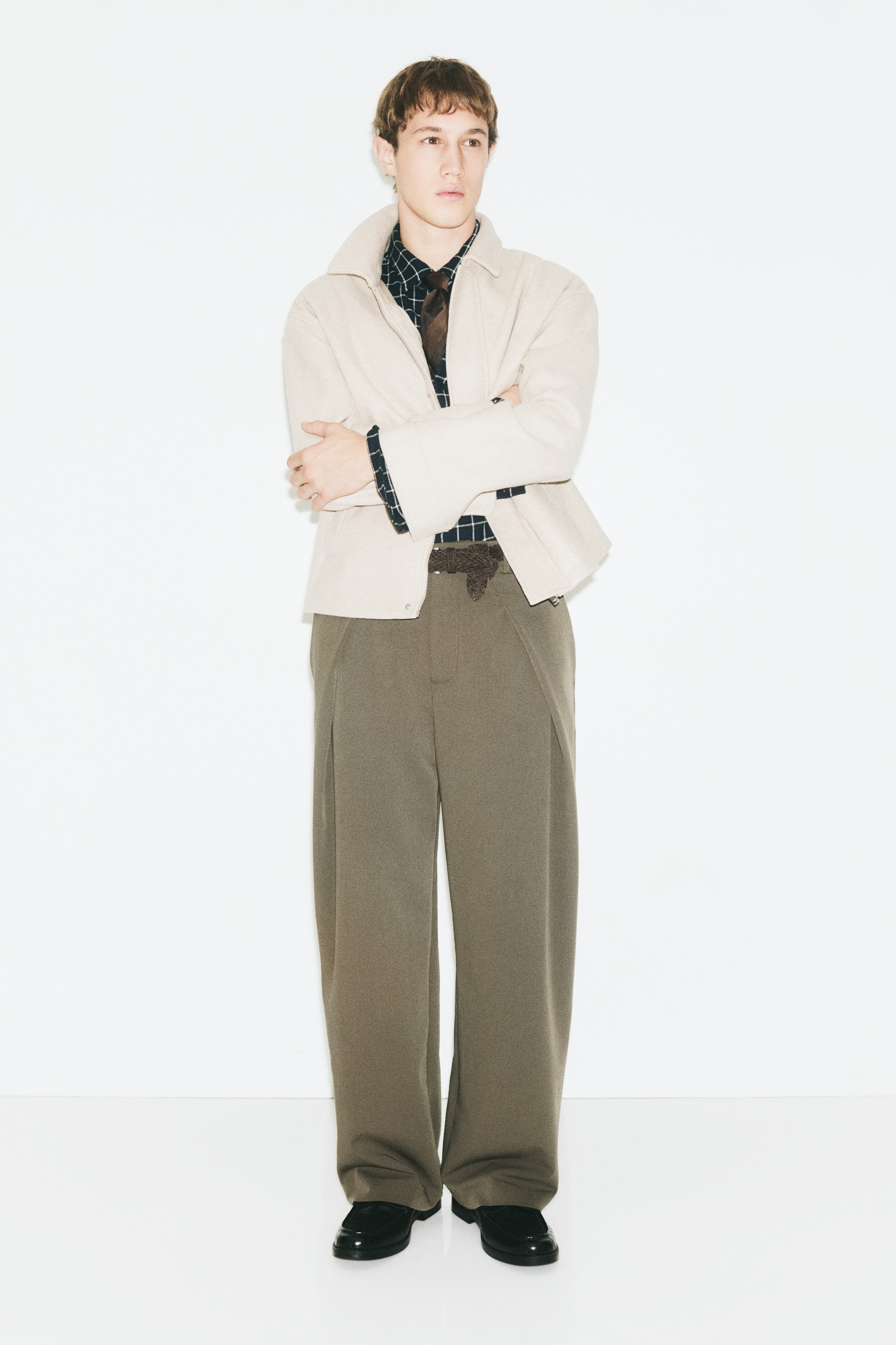 These brown wide-leg trousers are hanging facing forward, featuring a structured waistband with belt loops and a concealed front fly. They showcase deep, dramatic single pleats on each side, which drape into a relaxed, straight-leg silhouette.