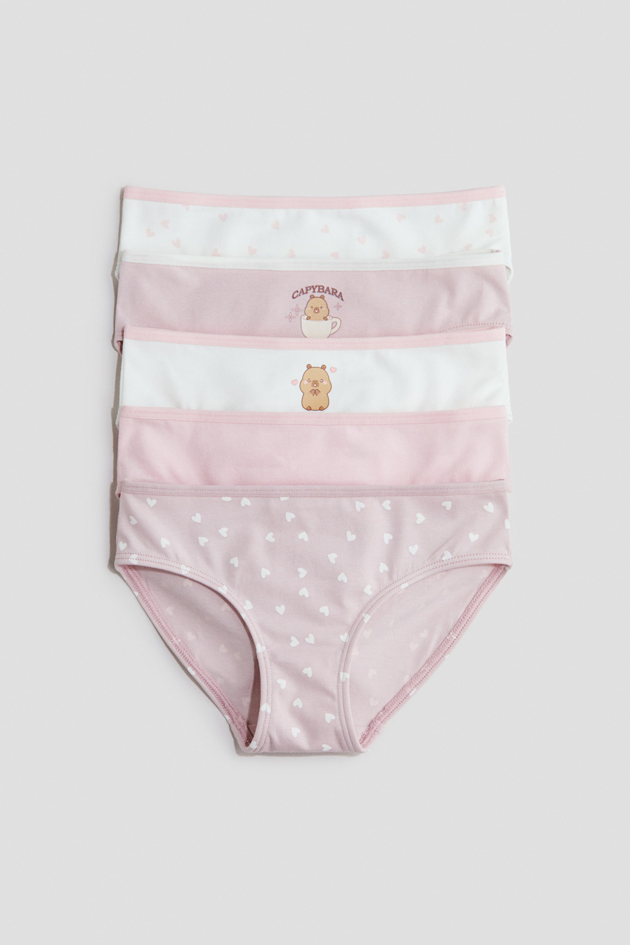 Visualizza l'immagine ingrandita: Cinque slip in jersey di cotone sono impilati verticalmente, rivolti verso il fronte, mostrando un mix di rosa chiaro tinta unita, motivi a cuori e grafiche di capibara. Ogni paio presenta una vita elasticizzata e un piccolo fiocco decorativo in raso al centro davanti.