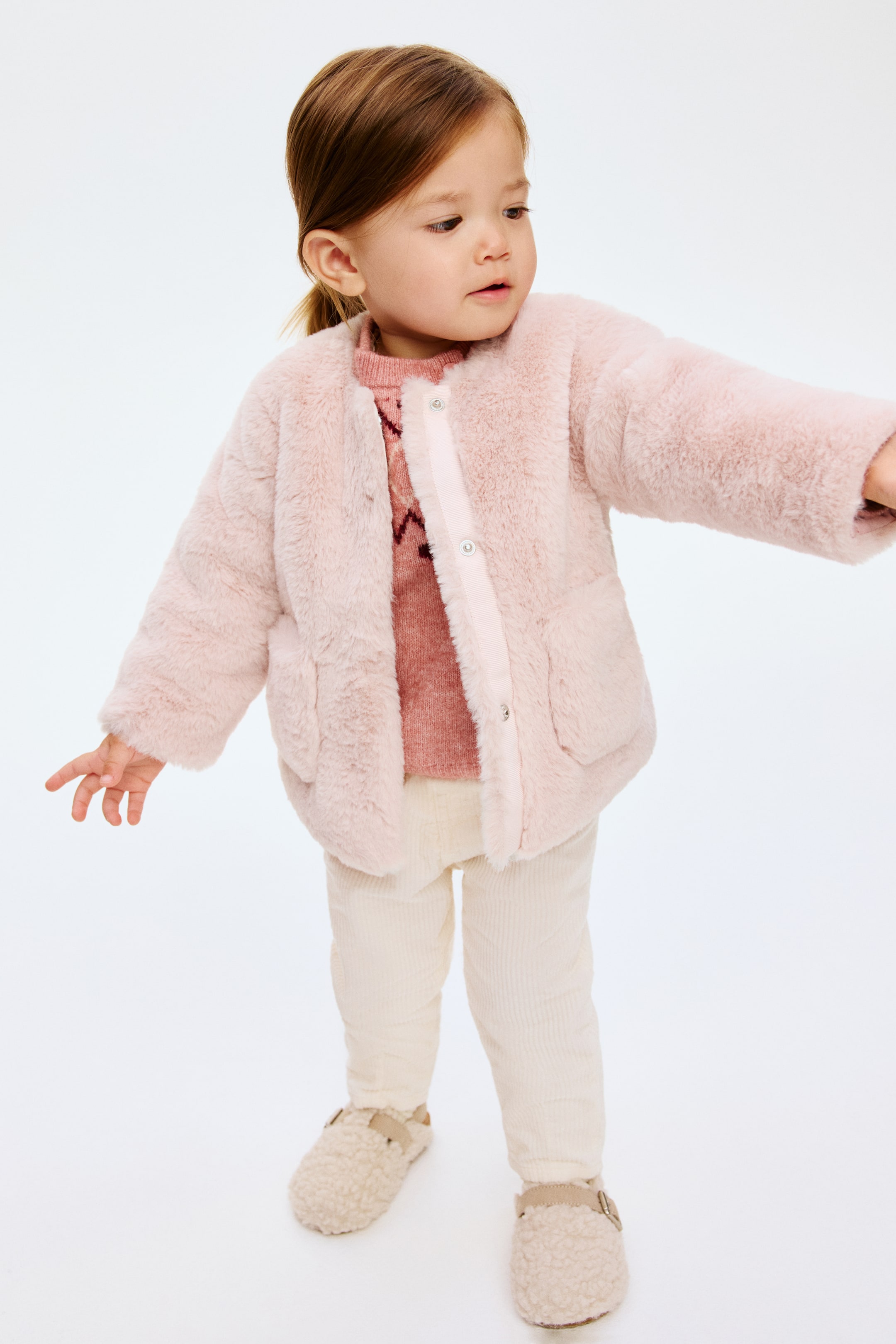 Grotere afbeelding bekijken: VOORKANT: Een roze jas in pluizige stof met een ronde halslijn en zichtbare drukknopen op een voorlijst. Het toont ook open voorzakken, met een roze gebreide trui die eronder zichtbaar is.
