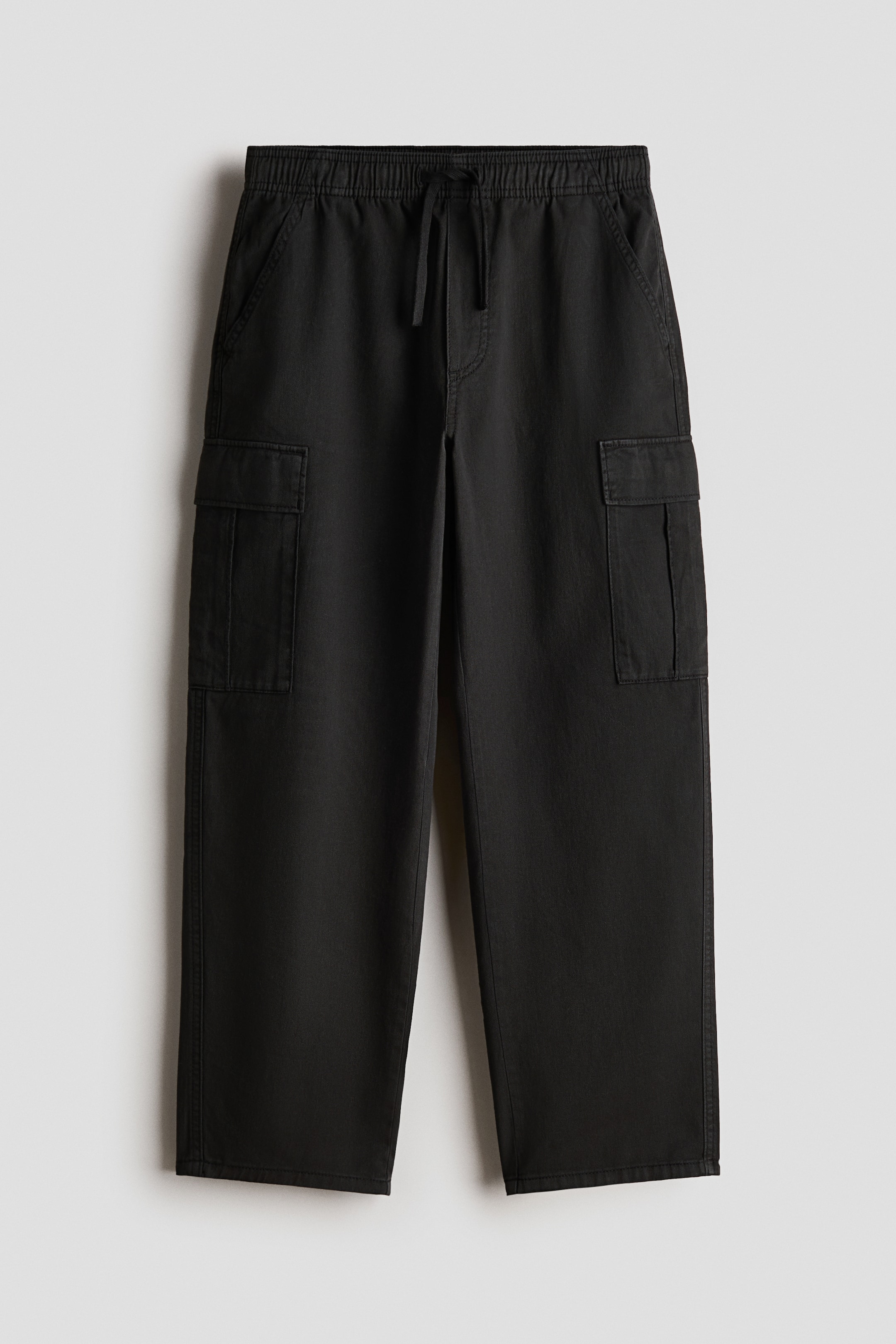 Größeres Bild anzeigen: Schwarze, locker sitzende Hosen in Vorderansicht, mit einem elastischen Kordelzugbund, diagonalen Seitentaschen und Blasebalg-Beintaschen mit Klappen an den konisch zulaufenden Beinen.