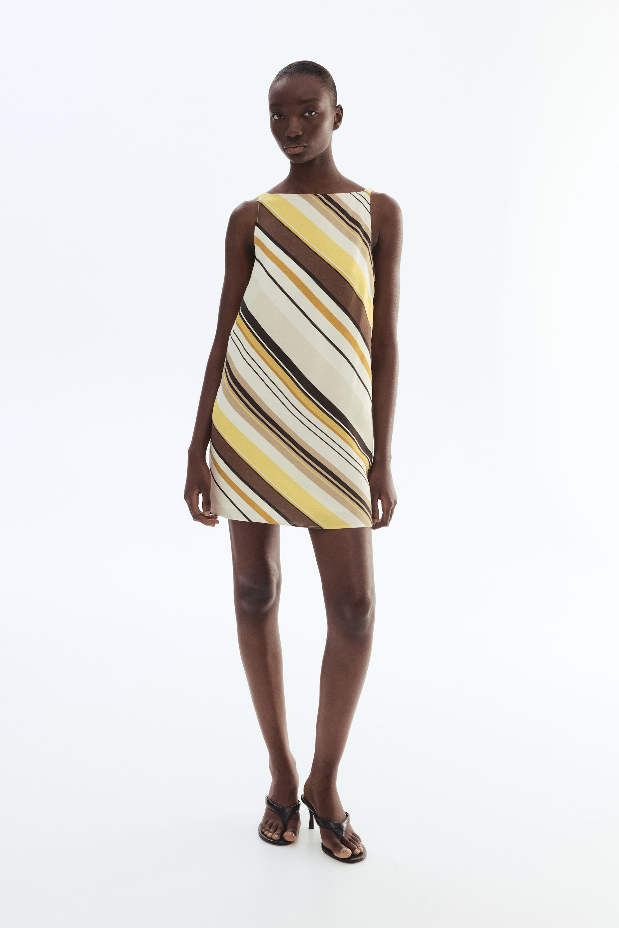 View larger image: A sleeveless mini dress featuring a diagonal stripe pattern in shades of yellow, brown, black, and cream, presenting a straight silhouette with a boat neckline and ending above the knee.