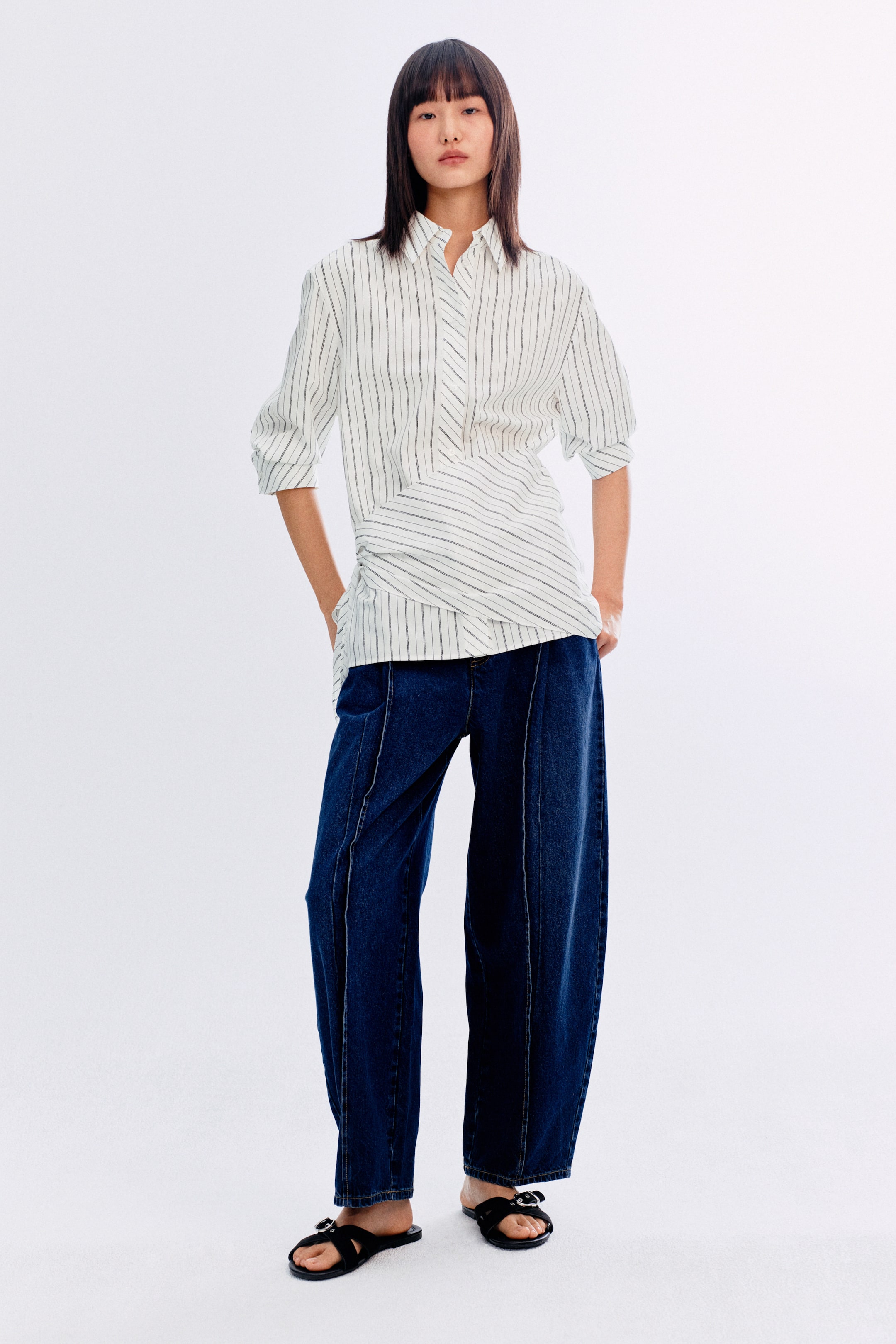 이미지 확대 보기: 앞면으로 보여지는 흰색과 검은색 줄무늬의 칼라 셔츠는 버튼업 플래킷과 3/4 소매를 특징으로 합니다. 셔츠 디자인은 상단 부분에 수직 줄무늬가 있으며, 허리 부분에는 비대칭 랩 디테일과 대각선 줄무늬로 전환됩니다.