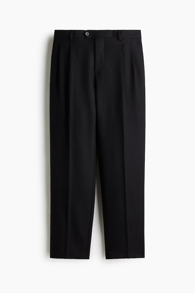 Black trousers are presented from the front, featuring a button and zip closure, belt loops, and double pleats on each leg. A sharp center crease is running down the front of both legs. - 1