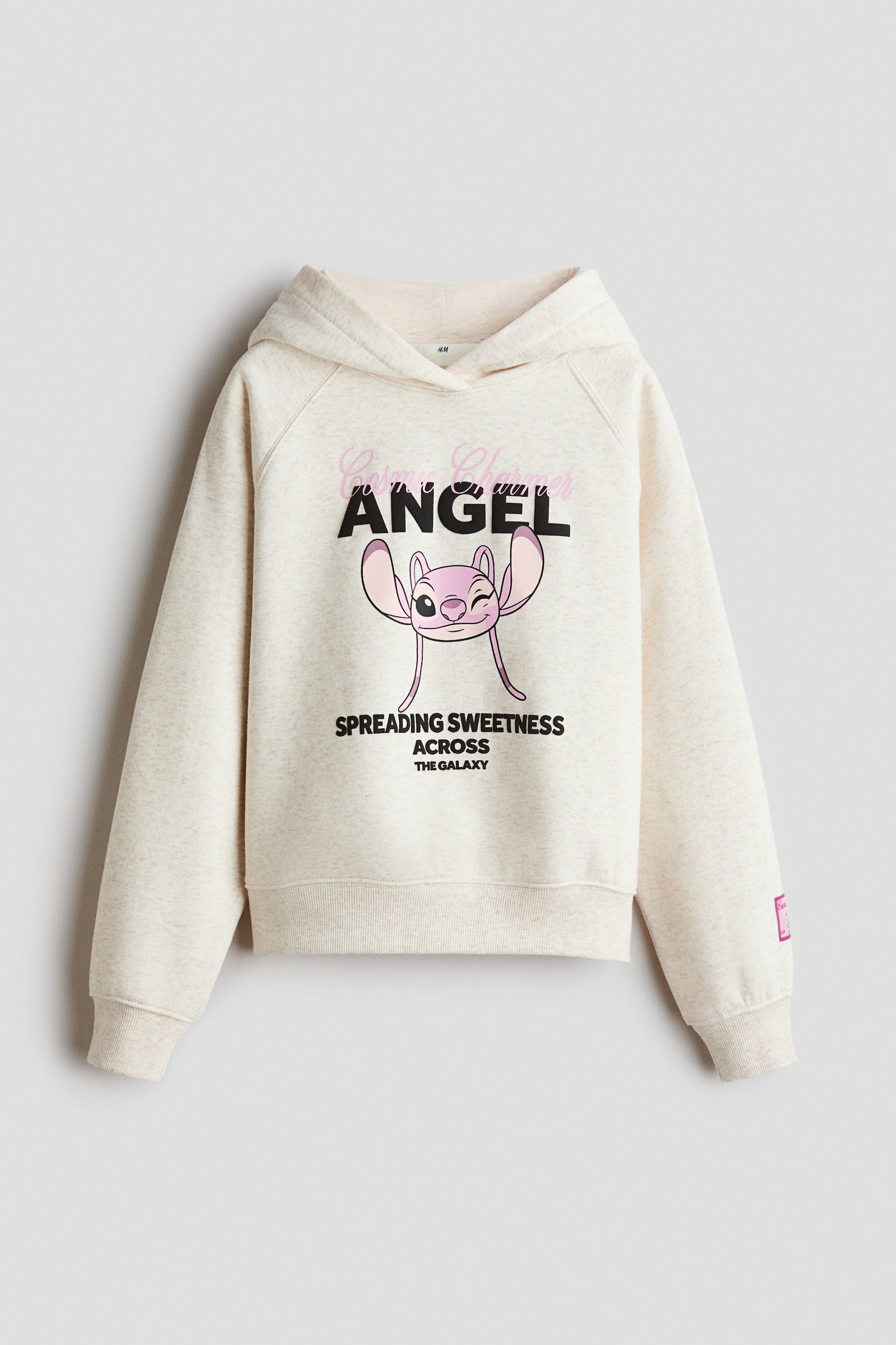 Ver imagen más grande: Se muestra una sudadera con capucha de corte oversize en tejido polar afelpado de color beige claro, vista de frente, con capucha de diseño cruzado y mangas raglán largas. En la zona del pecho luce un gráfico estampado de un personaje de dibujos animados rosa con texto, mientras que un amplio acabado de canalé remata los puños y el bajo.