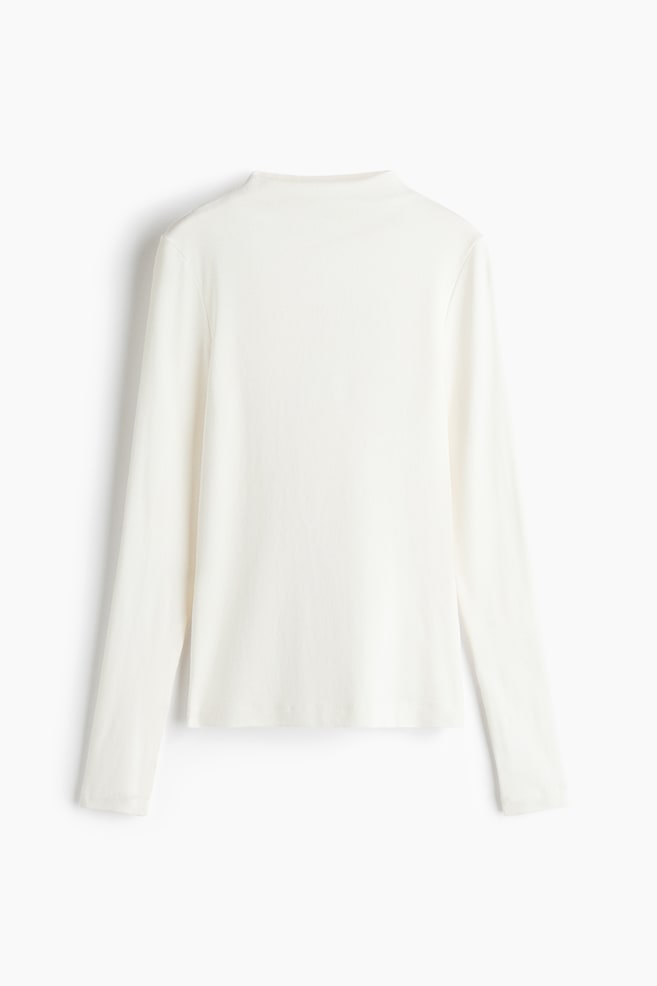 A long-sleeved, high-neck top in soft, off-white jersey is displayed with a fitted silhouette from the front. The top features a mock neck, long straight sleeves, and a clean, straight hem. - 1