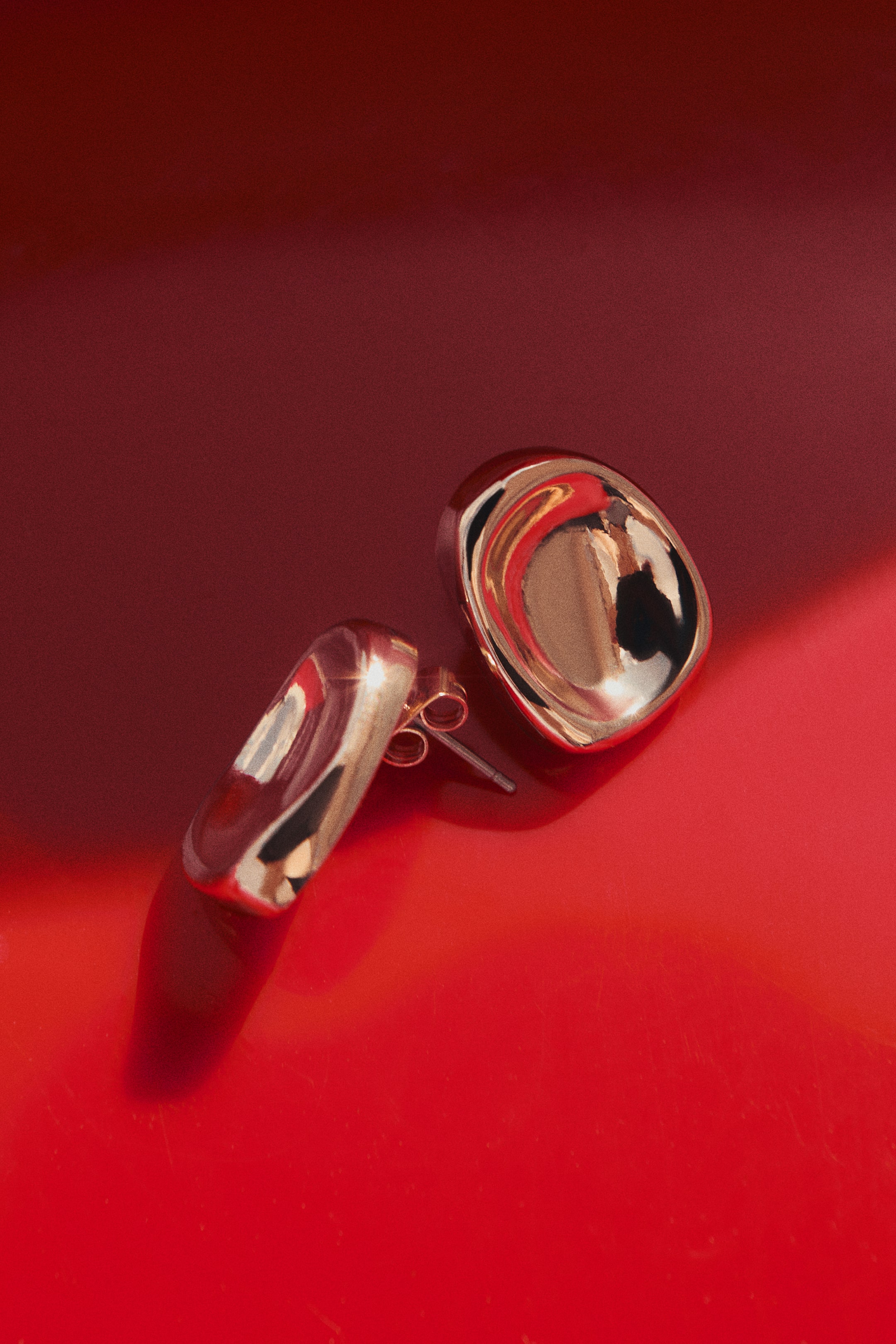 View larger image: Dome-shaped metal stud earrings showcase a highly polished, reflective finish with an organic, slightly concave design. One earring faces forward, highlighting its rounded, smooth contours, while the other rests on its side, revealing the post-back closure with a butterfly clutch.