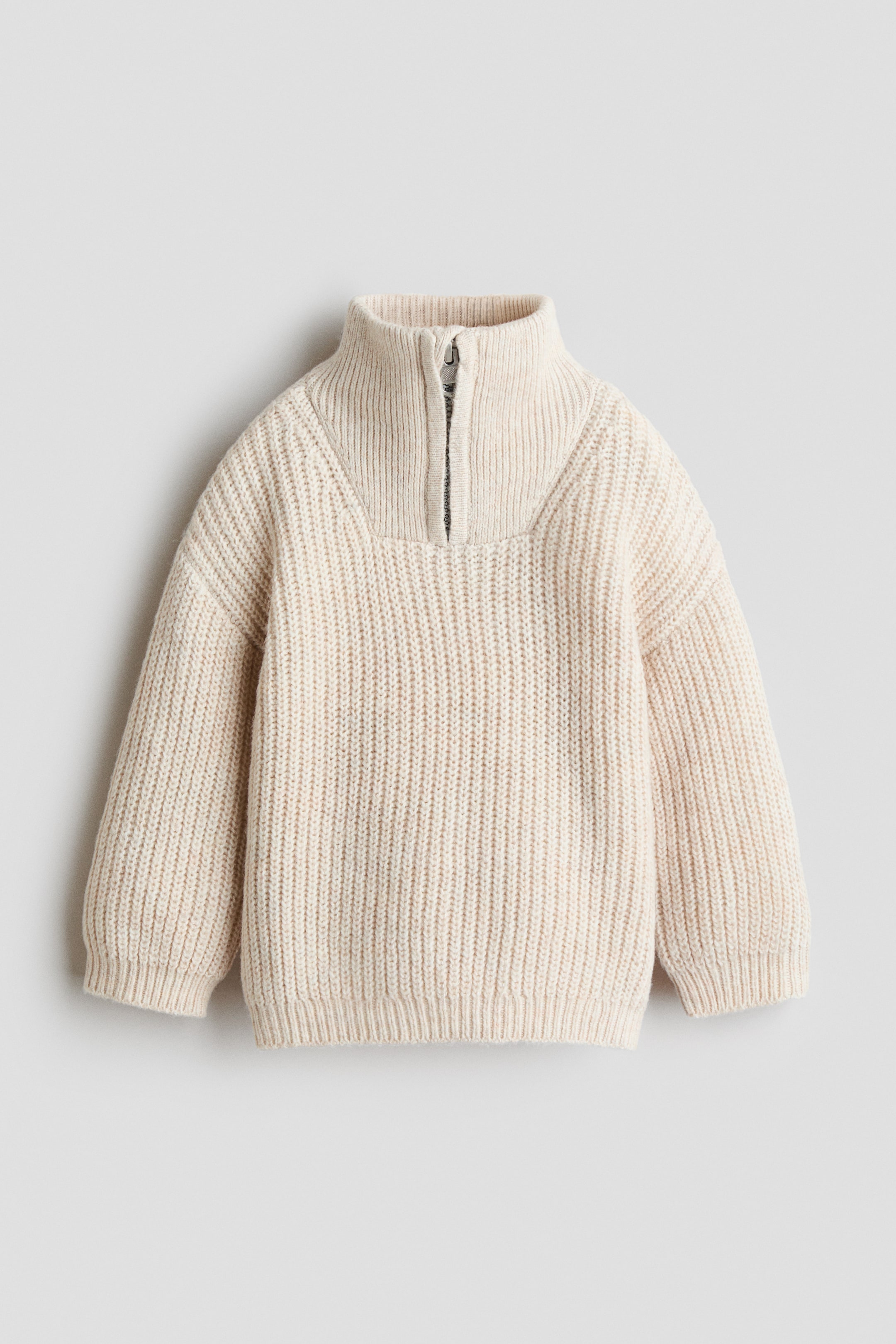 Ver imagen más grande: Un jersey de color blanco roto presenta un diseño de canalé, cuello alto con cremallera parcialmente abierta en la parte superior y hombros caídos, con puños y bajo finamente acanalados.