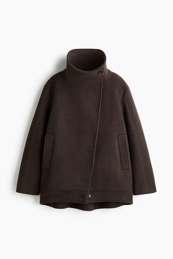Eine dunkelbraune Jacke aus Wollmischung ist von vorne zu sehen und zeigt einen hohen Stehkragen sowie einen asymmetrischen Frontknopfverschluss. Sie verfÃ¼gt Ã¼ber lange RaglanÃ¤rmel, vertikale Leistentaschen an den Seiten und einen leicht geschwungenen Saum. - 1