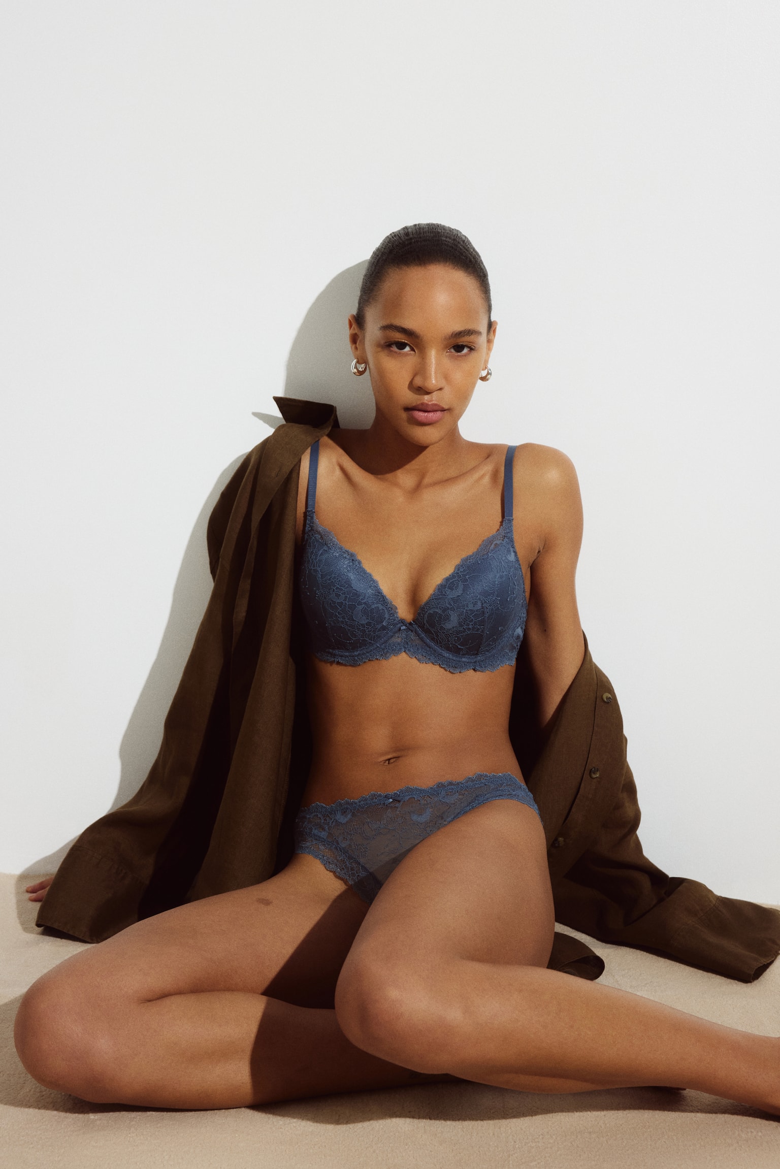 Two blue-grey lace thongs are laid flat, with one slightly overlapping the other, highlighting their front designs. Each thong features a delicate floral lace pattern and scalloped edges along the waist and leg openings. - 1