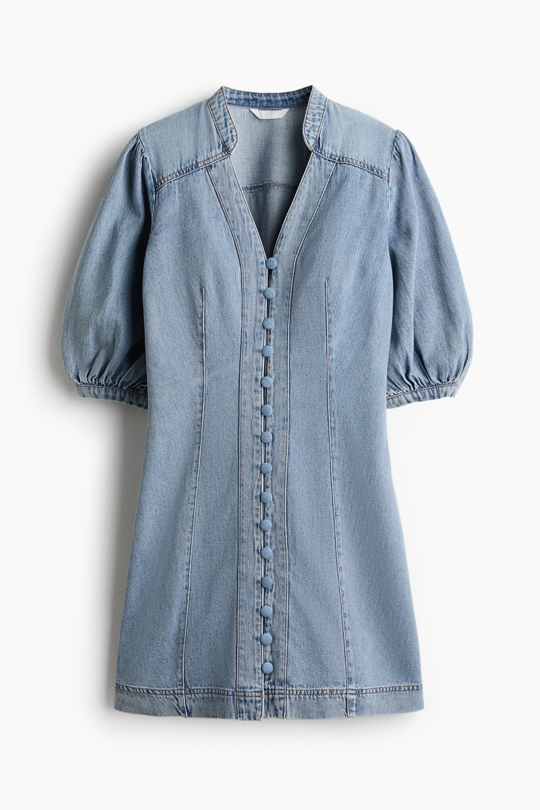 Se større billede: En kort, tætsiddende denimkjole er vist forfra og har en båndkrave og en V-formet åbning. Betrukne knapper løber ned langs fronten, mens korte voluminøse pufærmer med smalle manchetter, et skulderbærestykke og indsnit i taljen foran definerer dens tætsiddende pasform.