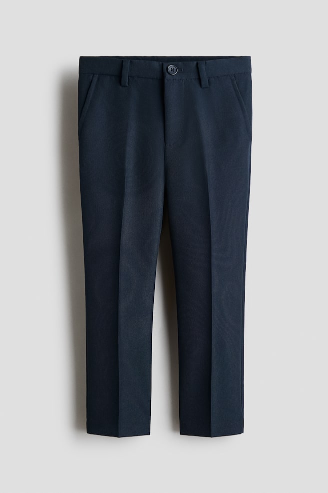 Marineblauwe broek met een platte voorkant. Ze hebben een enkele donkere knoopsluiting bij de tailleband, schuine zijzakken en rechte pijpen met opvallende vouwen die over de voorkant lopen. - 1