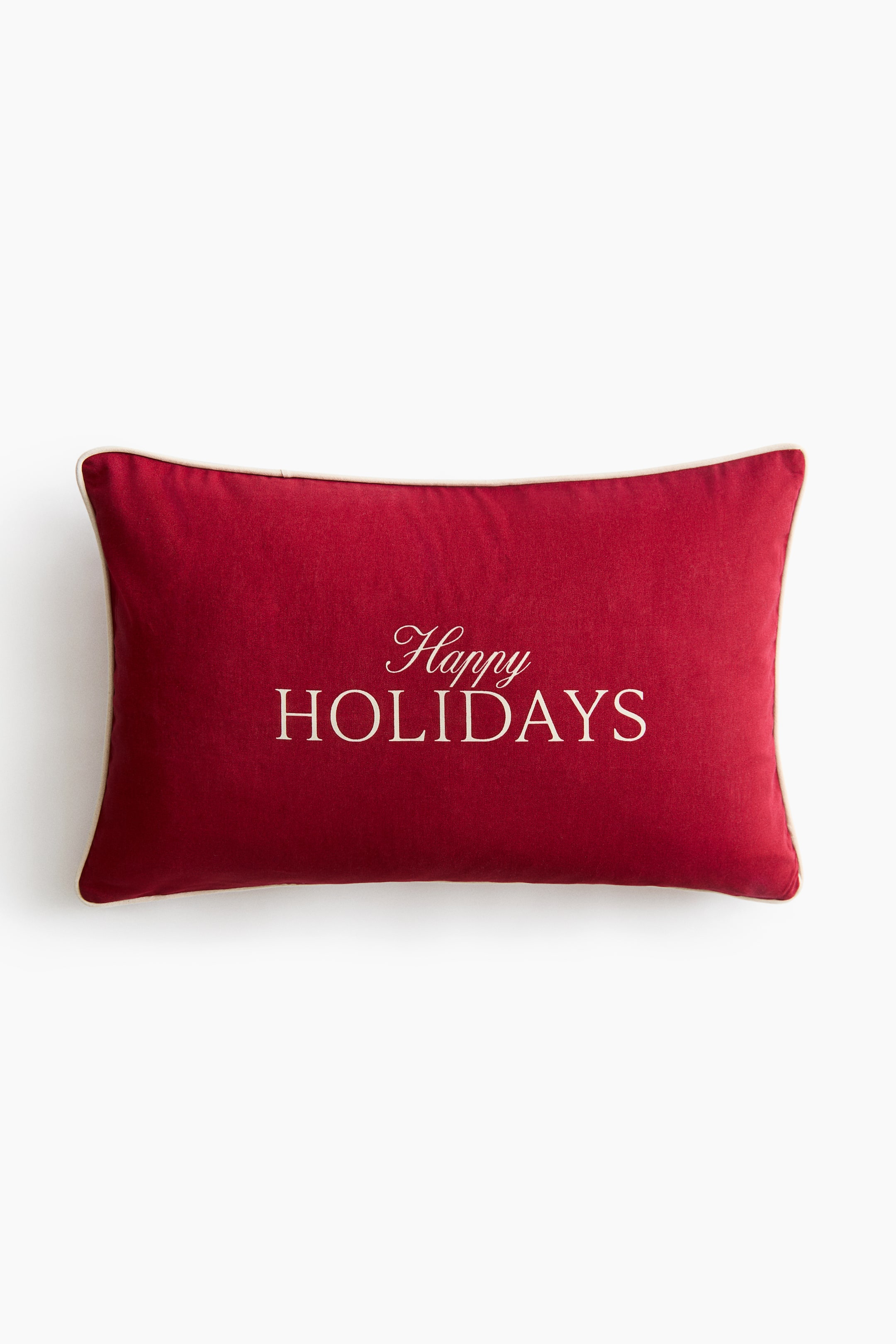 Se større billede: En rektangulær rød pyntepude ses forfra med ordene "Happy HOLIDAYS" broderet i en cremefarvet skrift midt på. Puden er afsluttet med matchende cremefarvet piping langs de ydre kanter.