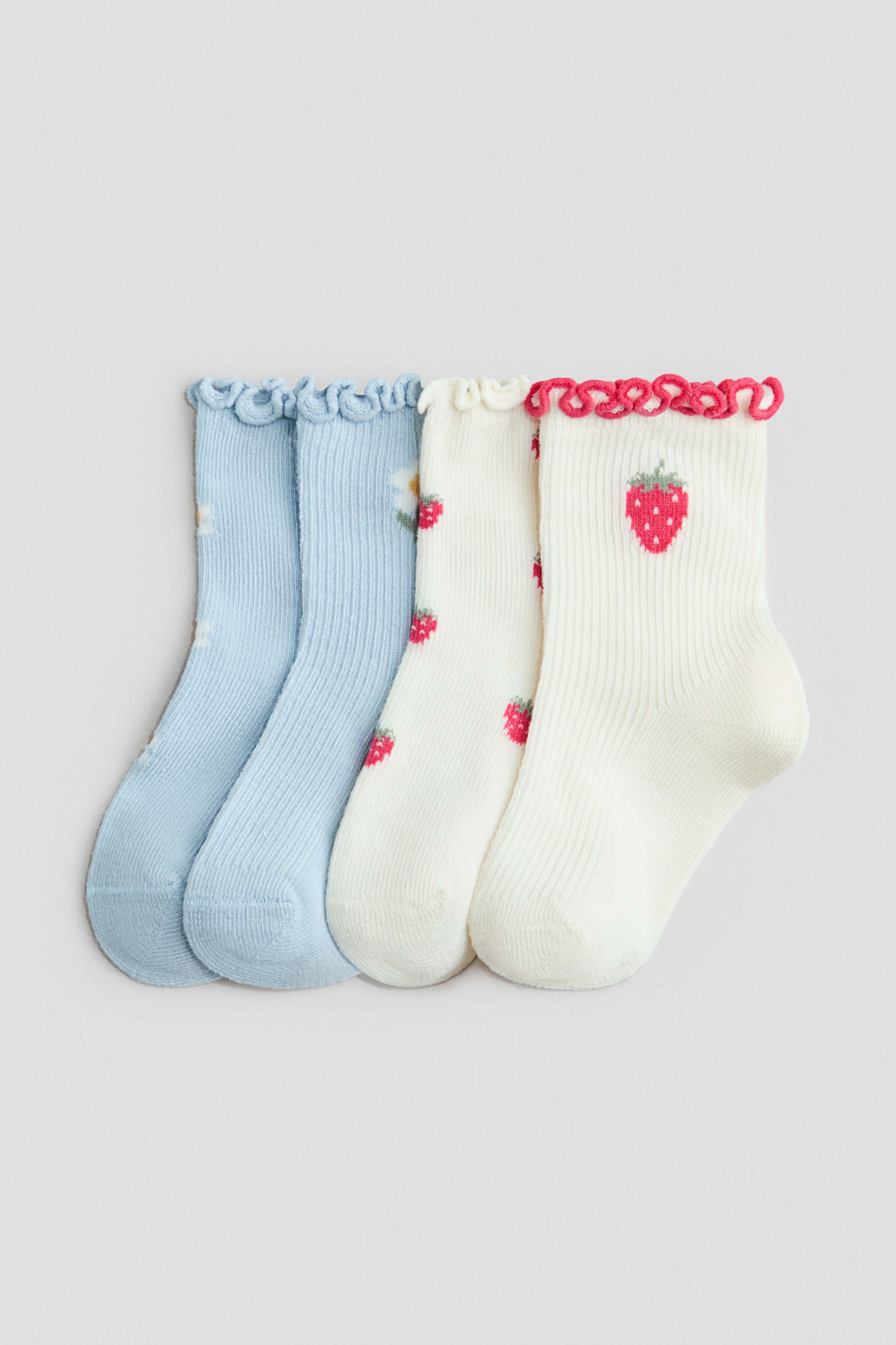 View larger image: Four ankle socks are positioned front-facing, arranged side by side. The two socks on the left are light blue, showcasing a ribbed texture, small white floral patterns, and light blue ruffled cuffs. The two socks on the right are off-white, exhibiting a ribbed texture, red strawberry patterns, and ruffled cuffs, with one cuff in off-white and the other in red.