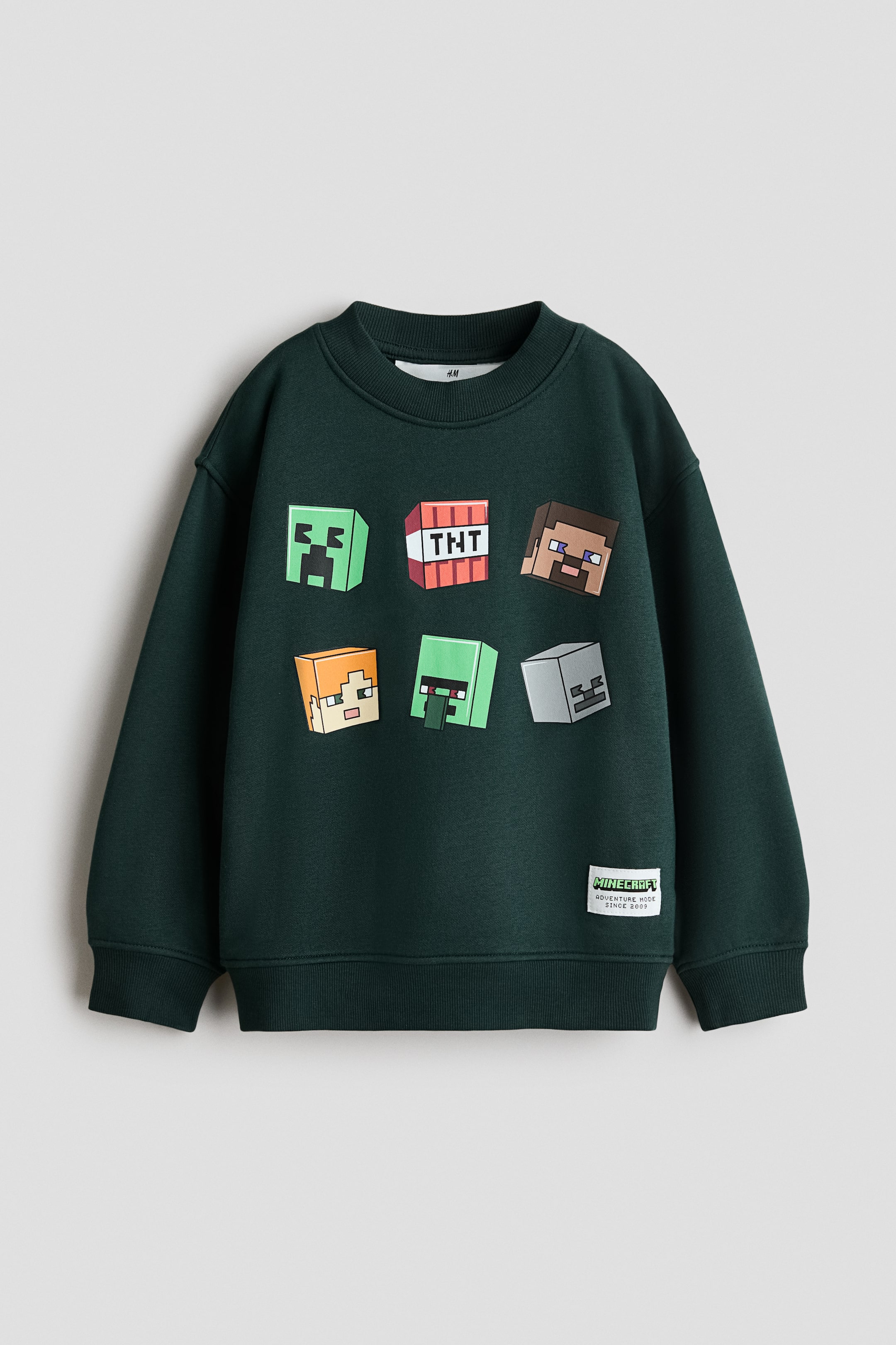 Visualizza immagine più grande: Una felpa girocollo verde scuro presenta la vista frontale, caratterizzata da sei stampe grafiche quadrate di personaggi e oggetti di Minecraft sul petto. È progettata con un girocollo a coste, maniche lunghe con polsini a coste e un orlo a coste, con un'etichetta tessuta bianca "Minecraft" cucita sul lato inferiore sinistro del davanti.