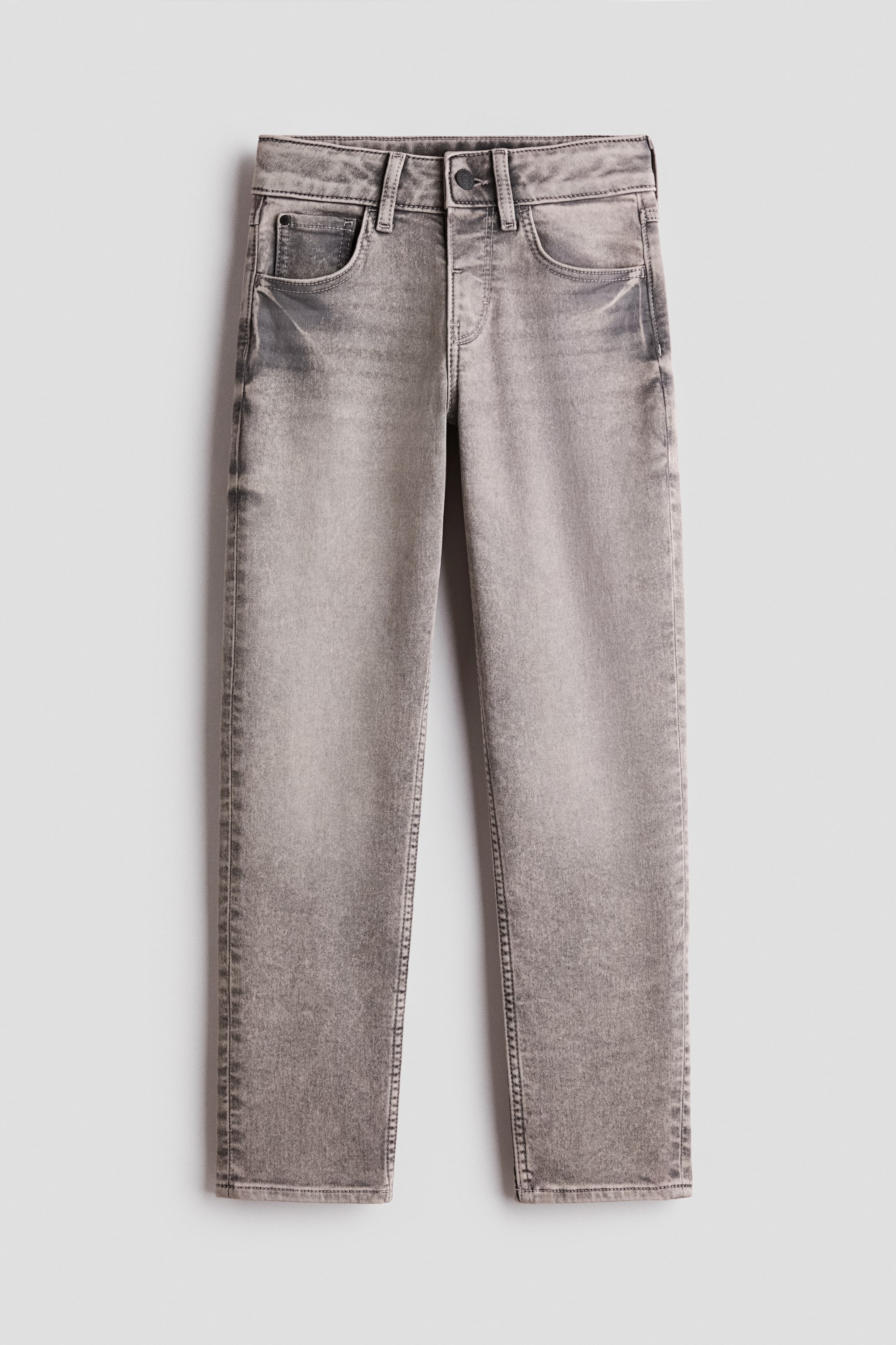 Agrandir l'image: Un jean en denim délavé gris est présenté à plat, de face. Il présente une fermeture à bouton, des passants de ceinture, deux poches avant et une poche monnaie, ainsi que des effets de délavage au niveau des cuisses et des genoux.