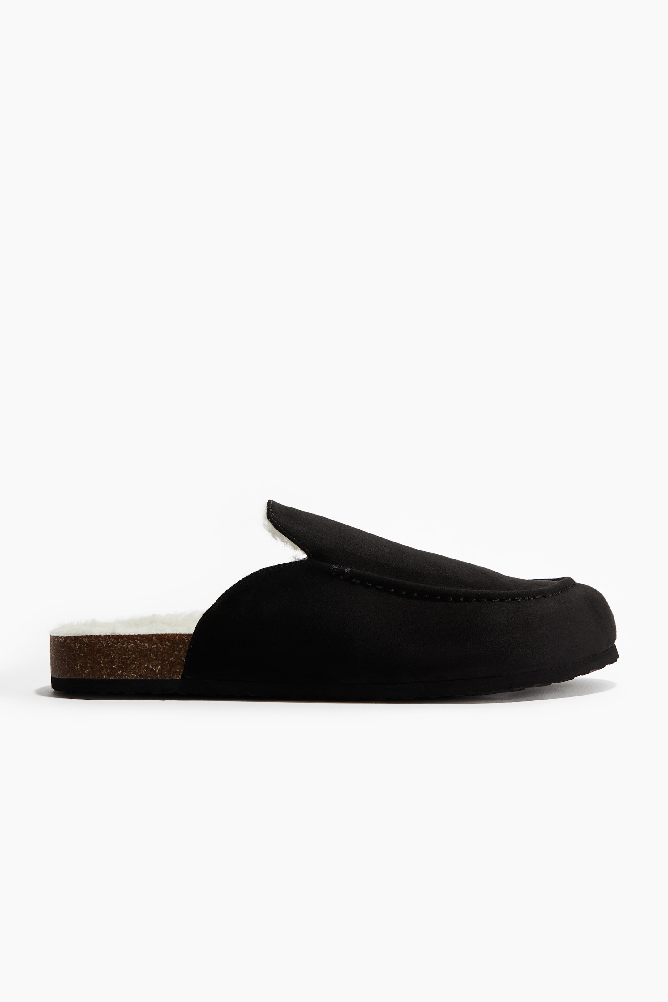 View larger image: A single black backless slipper is featuring a moccasin-style toe with visible stitching, a fluffy white lining that is visible along the top edge, and a cork-textured midsole with a dark outsole, displayed from a side profile.
