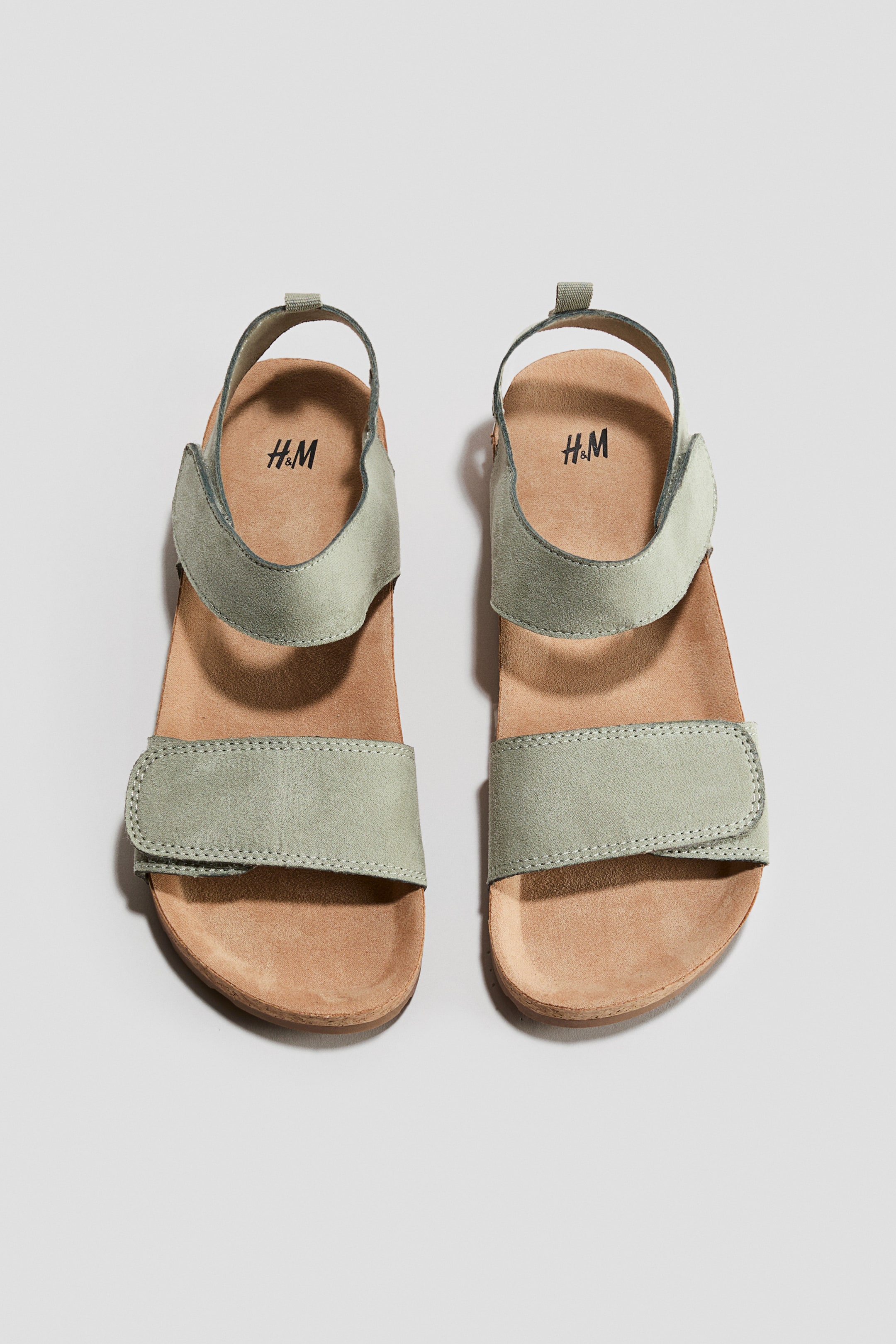 View larger image: A pair of sandals is facing forward, featuring a foot and ankle strap with a hook-and-loop fastening. The sandals feature moulded insoles, a loop at the back, and fluted soles.