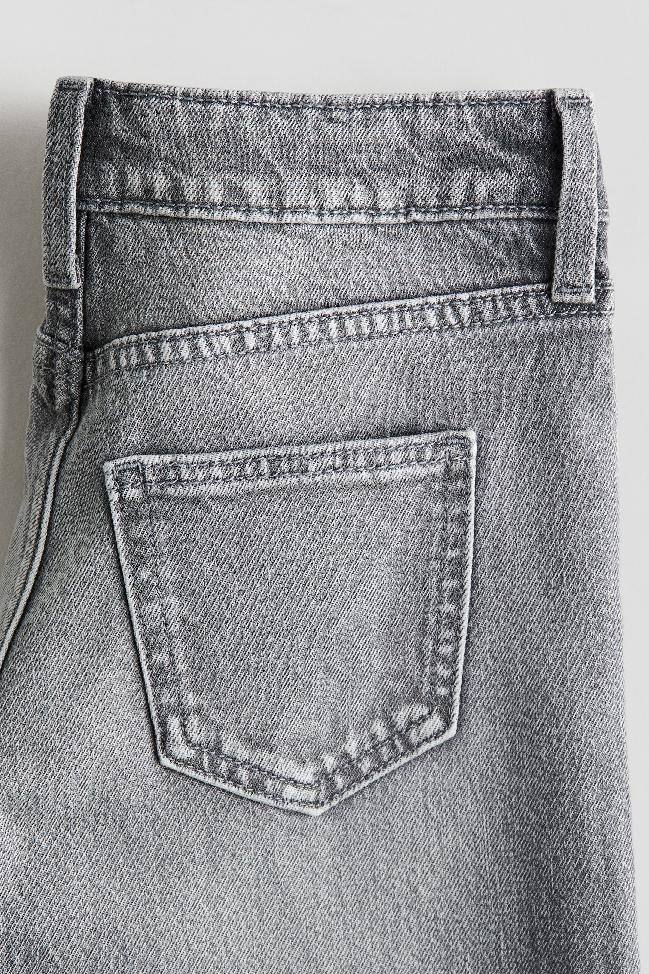View larger image: The back of gray denim jeans is being shown, featuring a washed-out look. A single back pocket is visible, detailed with prominent stitching, along with the top of the waistband and a belt loop.