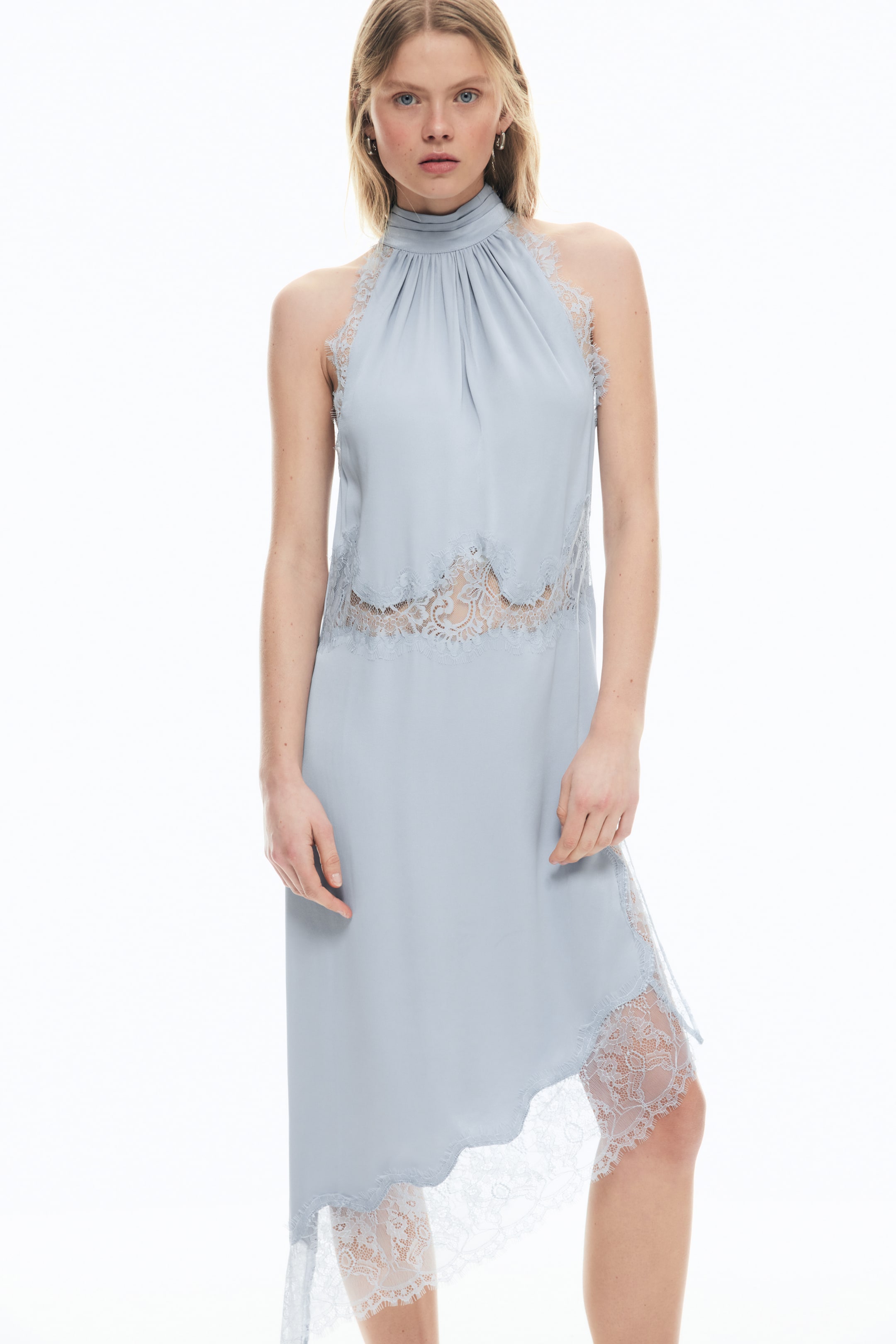 Größeres Bild anzeigen: Das hellblaue ärmellose Kleid zeichnet sich durch einen gerafften hohen Ausschnitt, Spitzenbesatz entlang des Ausschnitts und der Armlöcher, ein transparentes Spitzen-Midriff-Panel und einen asymmetrischen Saum mit zusätzlichen transparenten Spitzenakzenten aus.