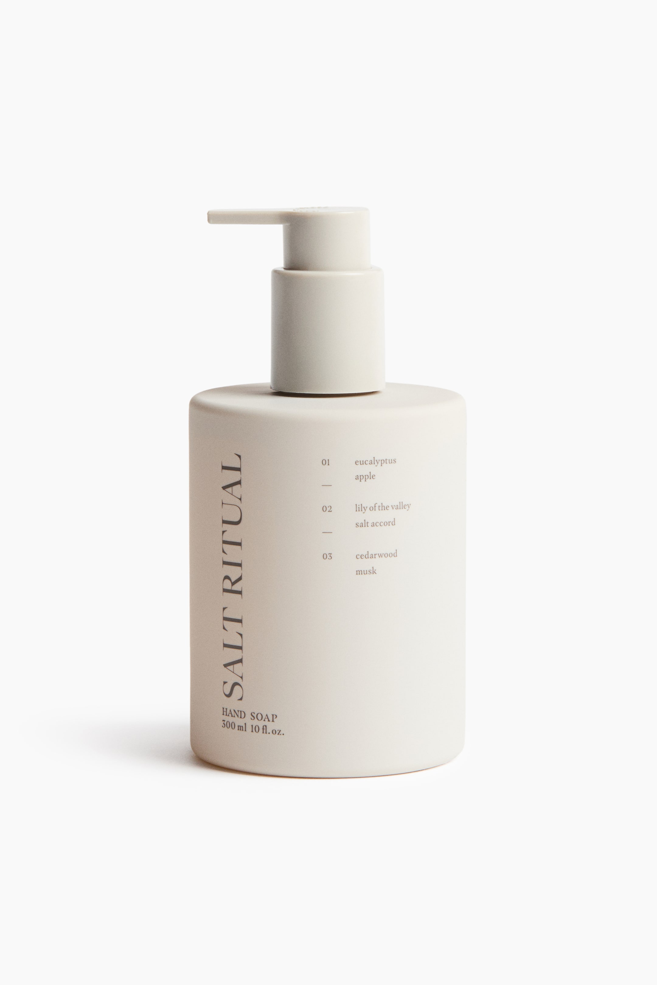 Ver imagen más grande: Una botella de jabón de manos de color beige claro, rectangular y con esquinas redondeadas, está de pie de frente, con un dispensador de bomba a juego en la parte superior. La botella muestra "Salt Ritual Hand Soap" y el texto de volumen en su lado inferior izquierdo, junto a una lista numerada de tres perfiles de aroma en su lado derecho.