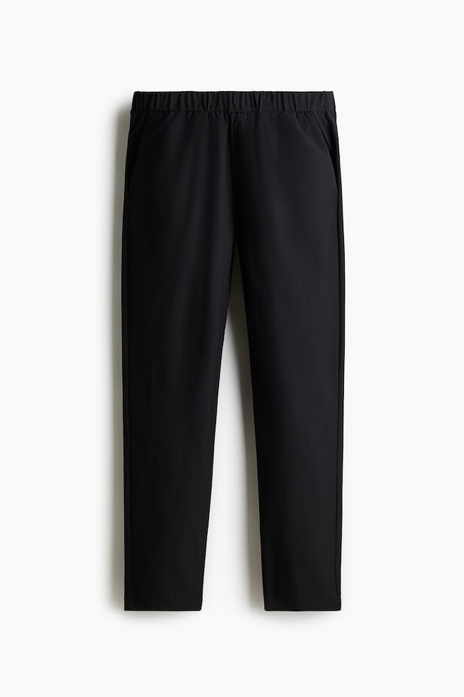 Schwarze Hosen werden von VORNE gezeigt, mit einem elastischen Bund und seitlichen Schlitztaschen, und präsentieren eine lockere, gerade Passform. - 1