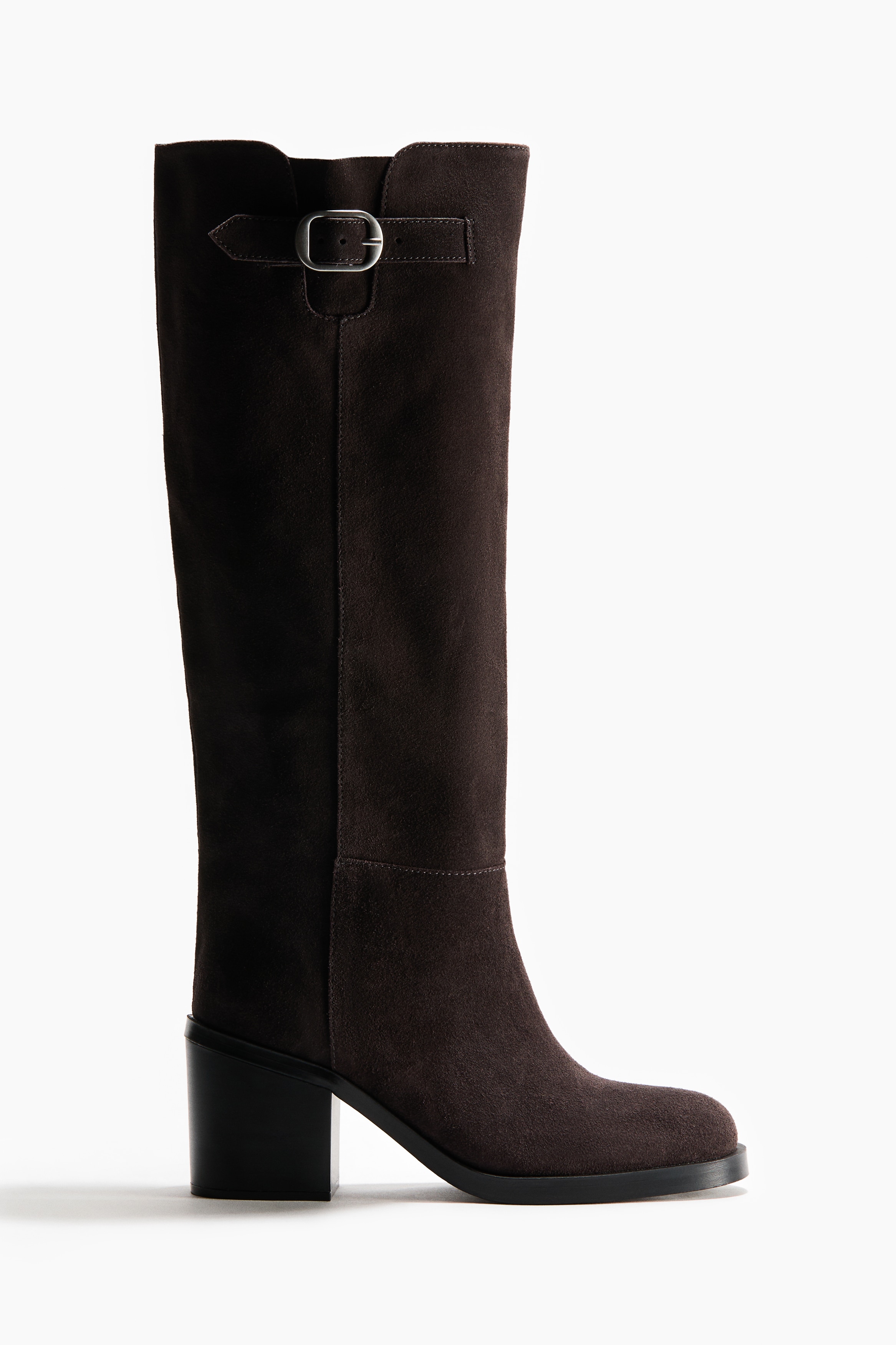 Knee-high boots in dark grey suede are being worn by the model, featuring rounded toes, dark green block heels, and a decorative tab with a silver-toned metal buckle at the top of the shaft. A beige knit garment is layered slightly over the top of the boot shaft.