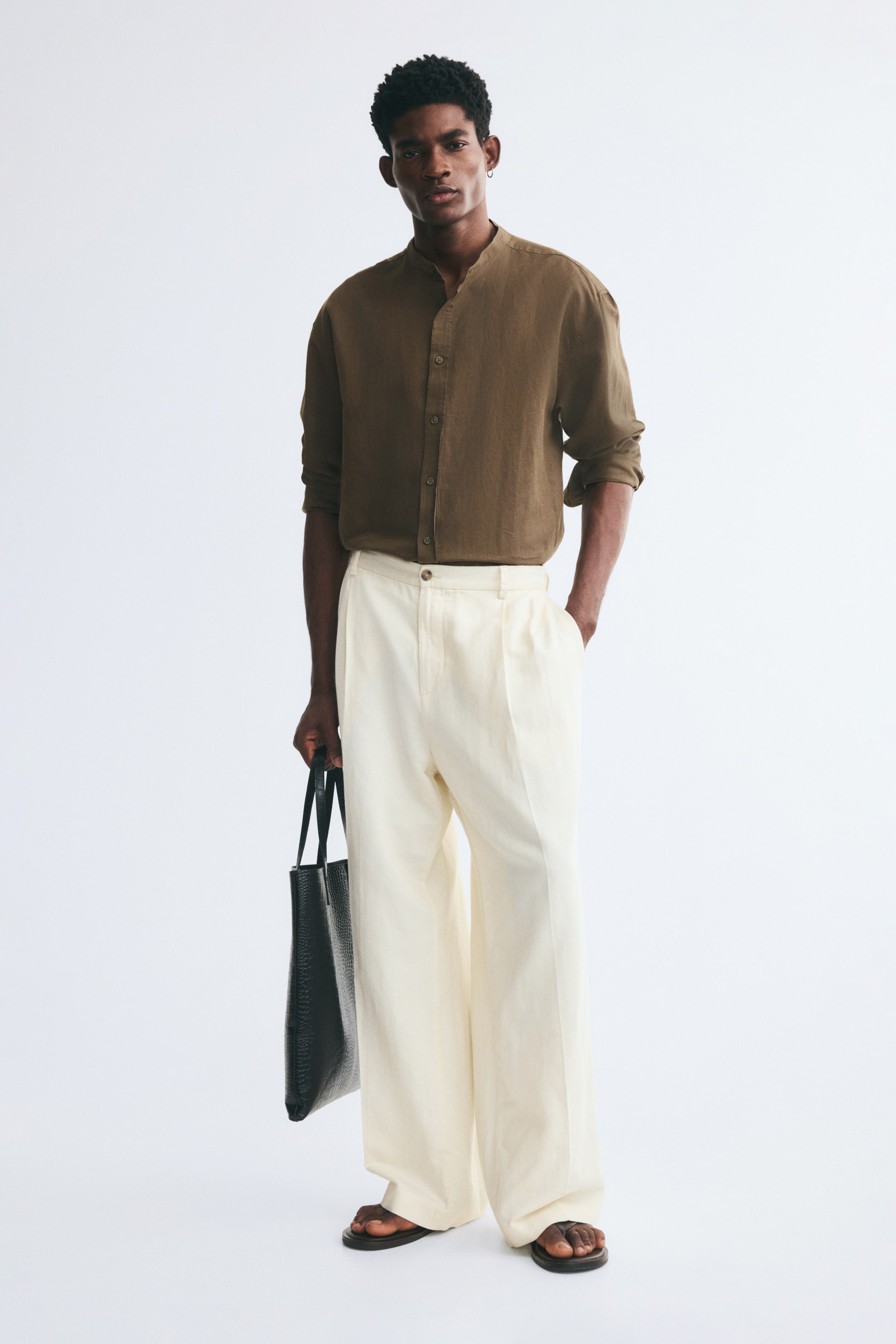 View larger image: A brown long-sleeved band-collar shirt in a textured linen-cotton blend is worn by the model, tucked into cream-coloured wide-leg trousers. The shirt features a button-up front and a relaxed fit, with the sleeves rolled up slightly at the forearms.