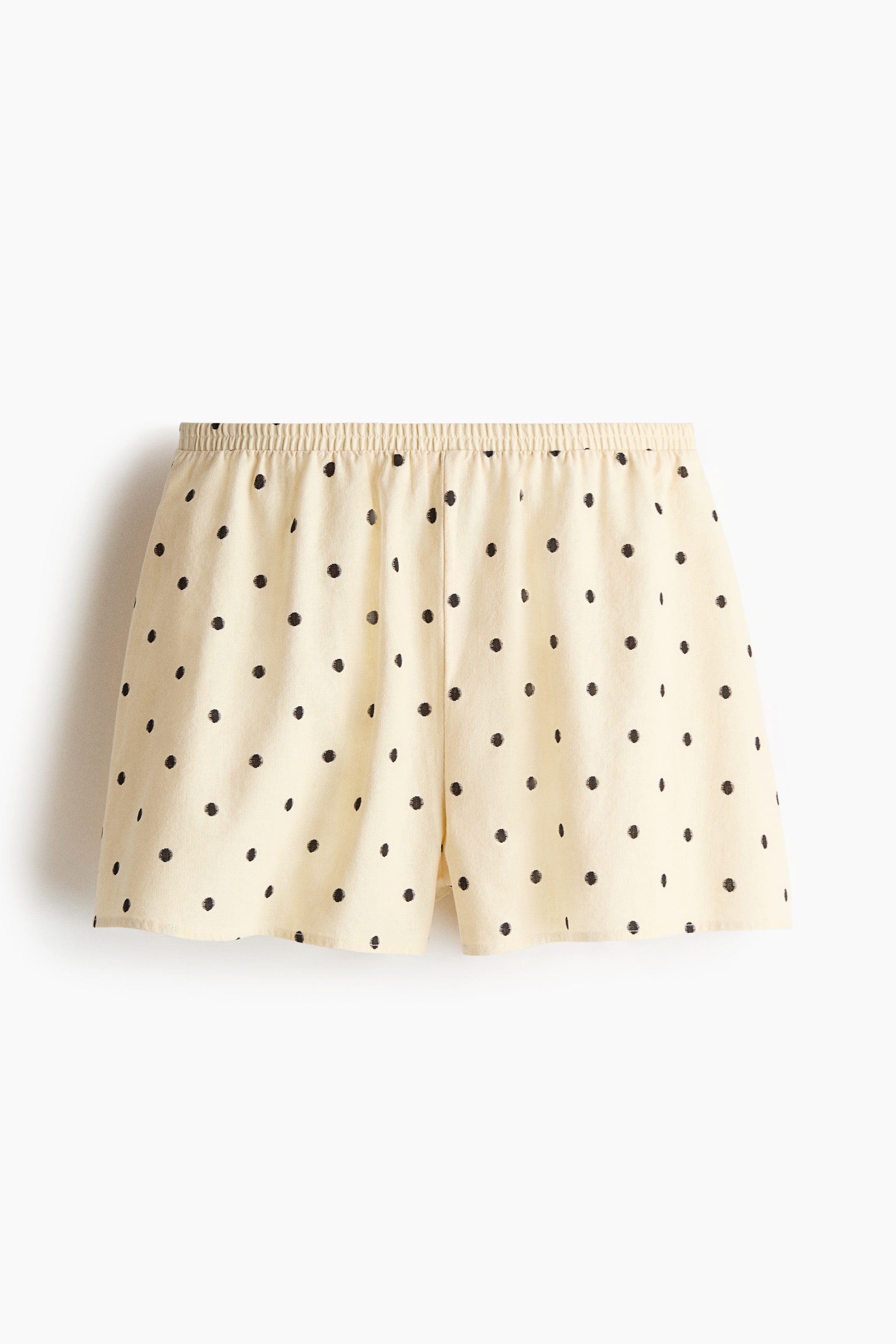Visualizza immagine più grande: Gli shorts sono mostrati frontalmente, in un tessuto color crema chiaro con pois neri sparsi, con vita elasticizzata e gamba ampia.