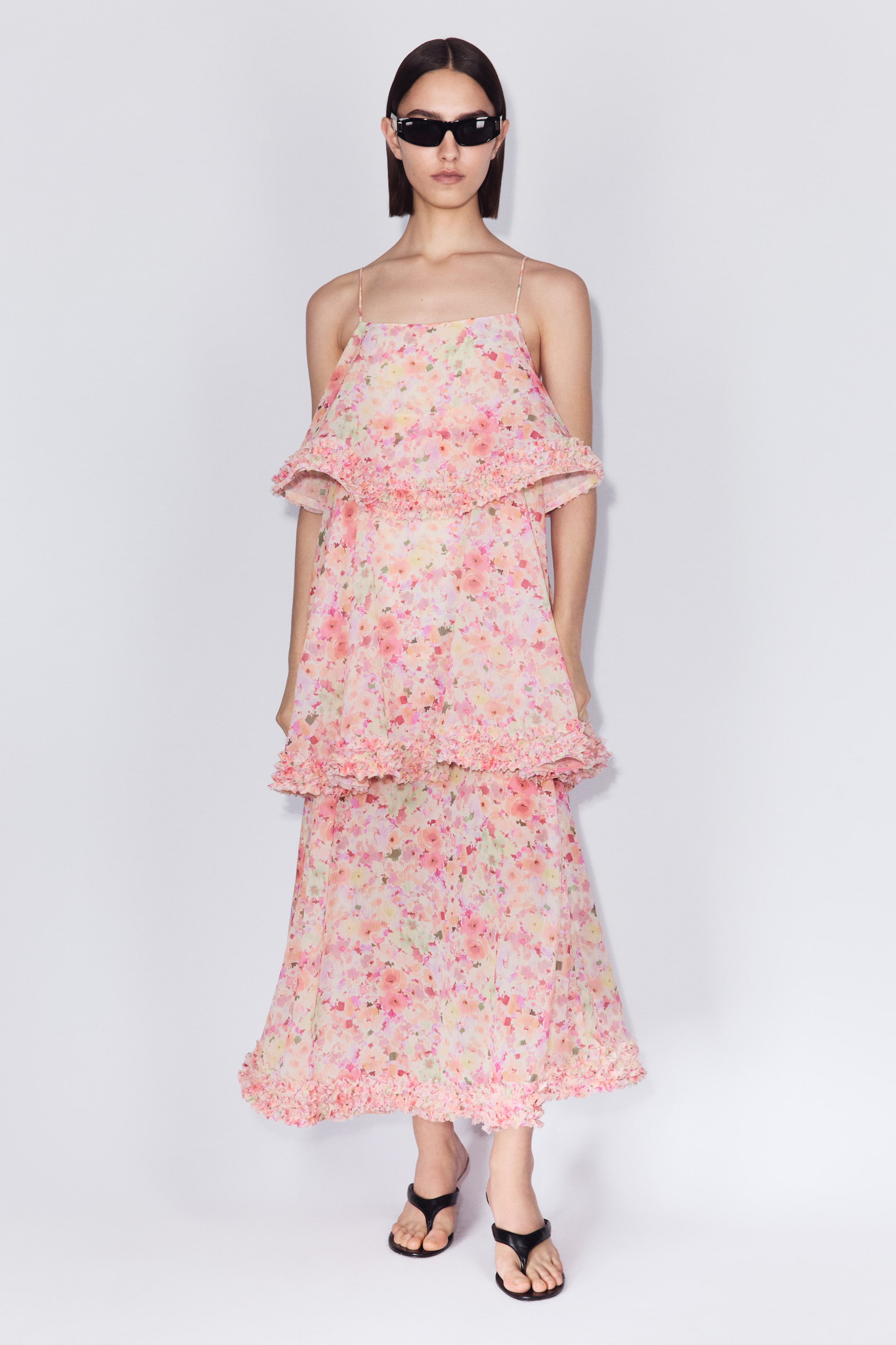View larger image: The model is wearing a long floral dress in pink, yellow, and green crinkled chiffon. It features a square neckline, spaghetti straps, and flounced tiers with ruffled edges.