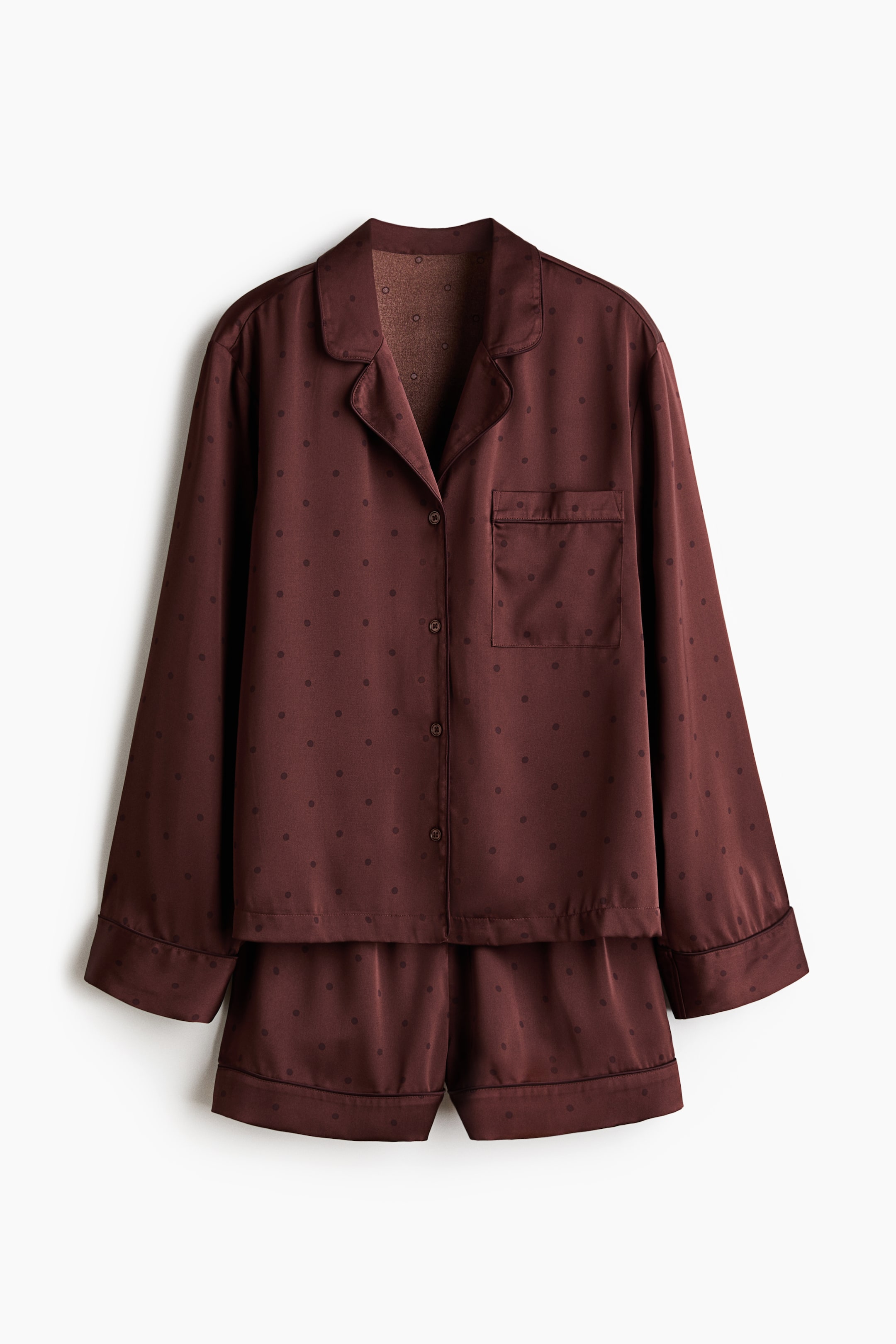 View larger image: A maroon pajama set menampilkan baju lengan panjang dan seluar pendek yang sepadan, kedua-duanya menampilkan corak titik polka yang halus dan kilauan lembut. Baju yang menghadap ke depan direka dengan lapel takuk, penutupan butang, dan satu poket tampal dada.