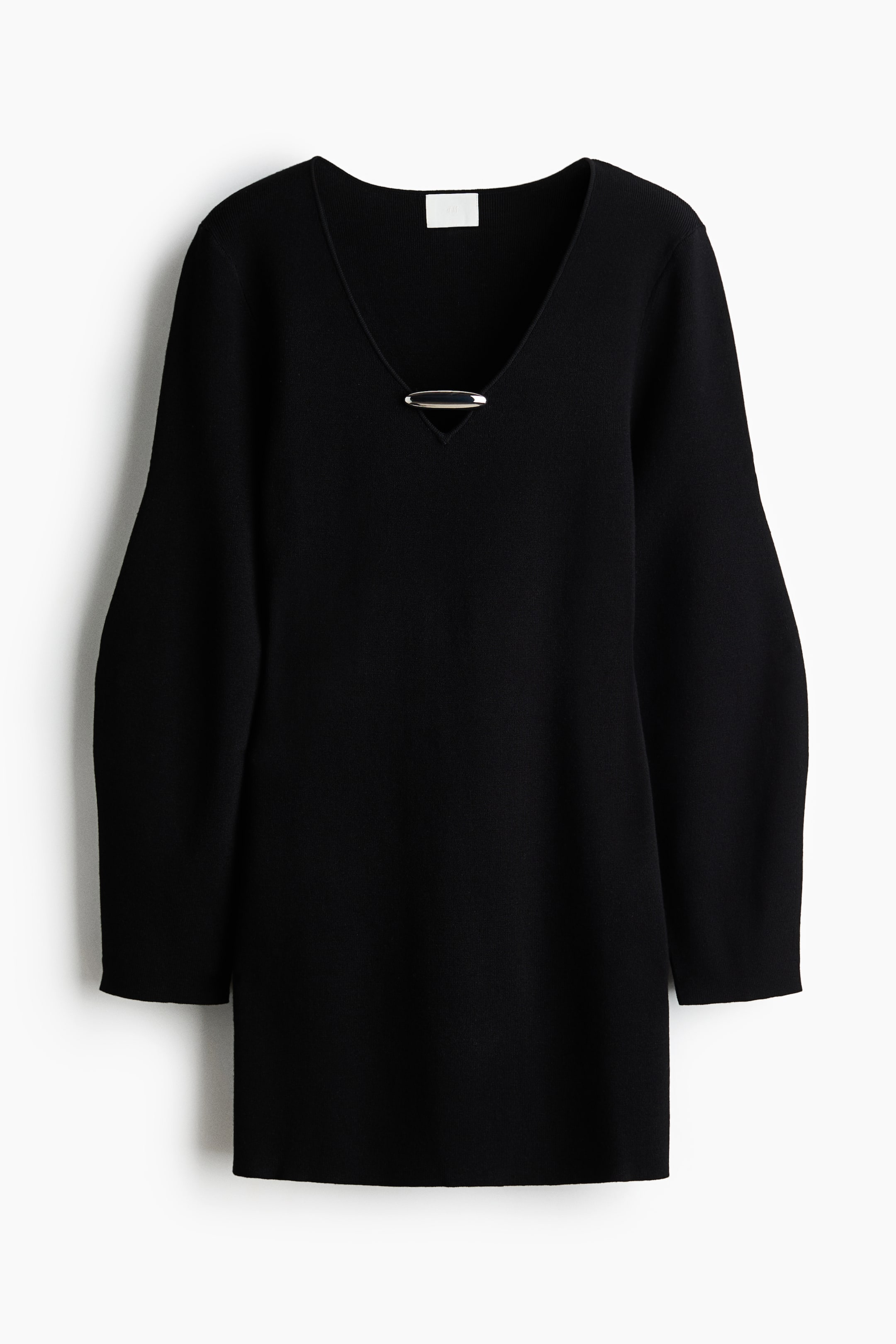 View larger image: A black knit dress is shown from the front, featuring a deep V-neckline with a horizontal silver-tone metal bar detail across the opening. The dress has long, relaxed-fit sleeves and a straight hemline in a smooth, fine-knit texture.