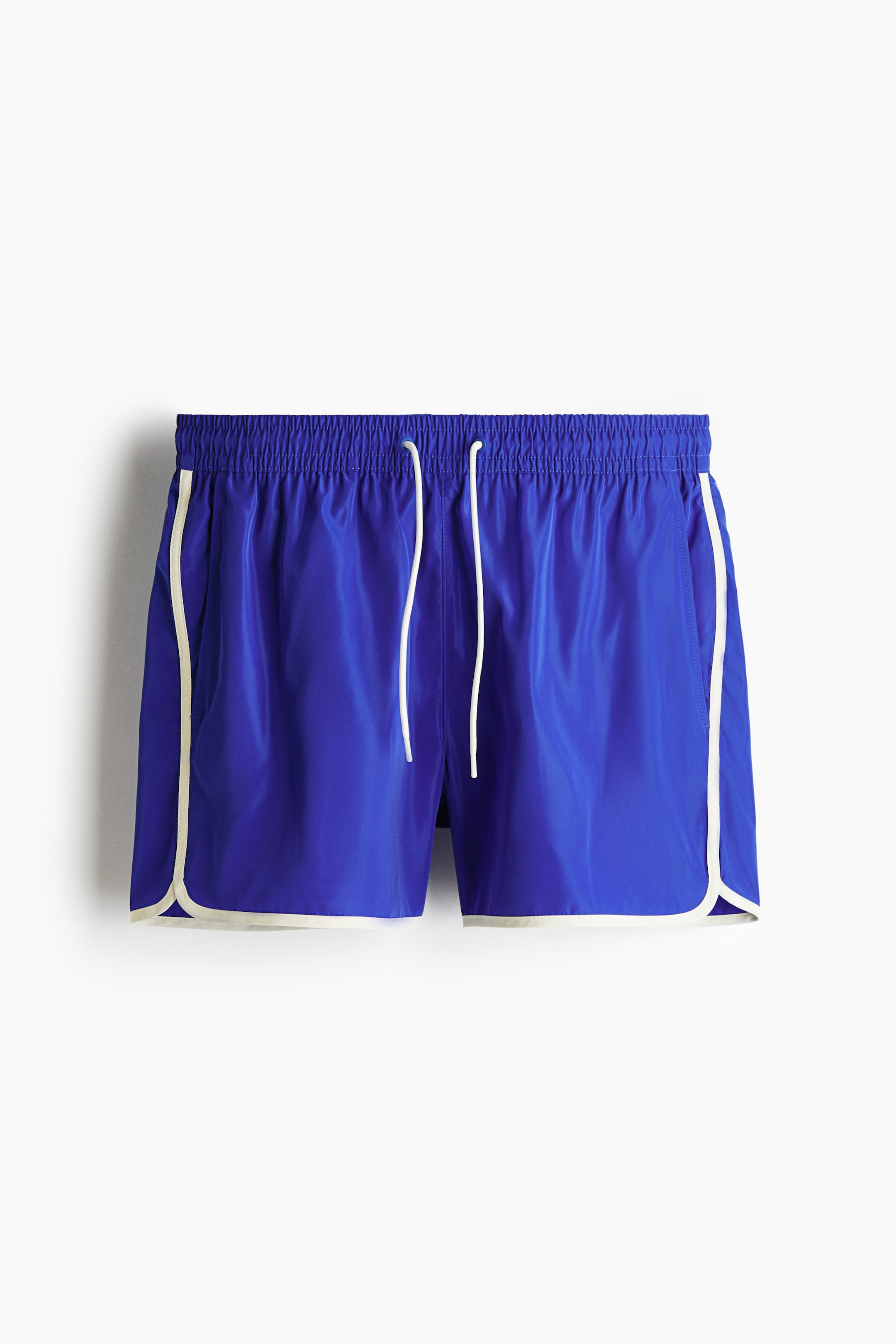 View larger image: Blue shorts are shown from the front, featuring a shirred elastic waistband with a white drawstring. Cream piping runs vertically along the side seams and curves around the leg openings.