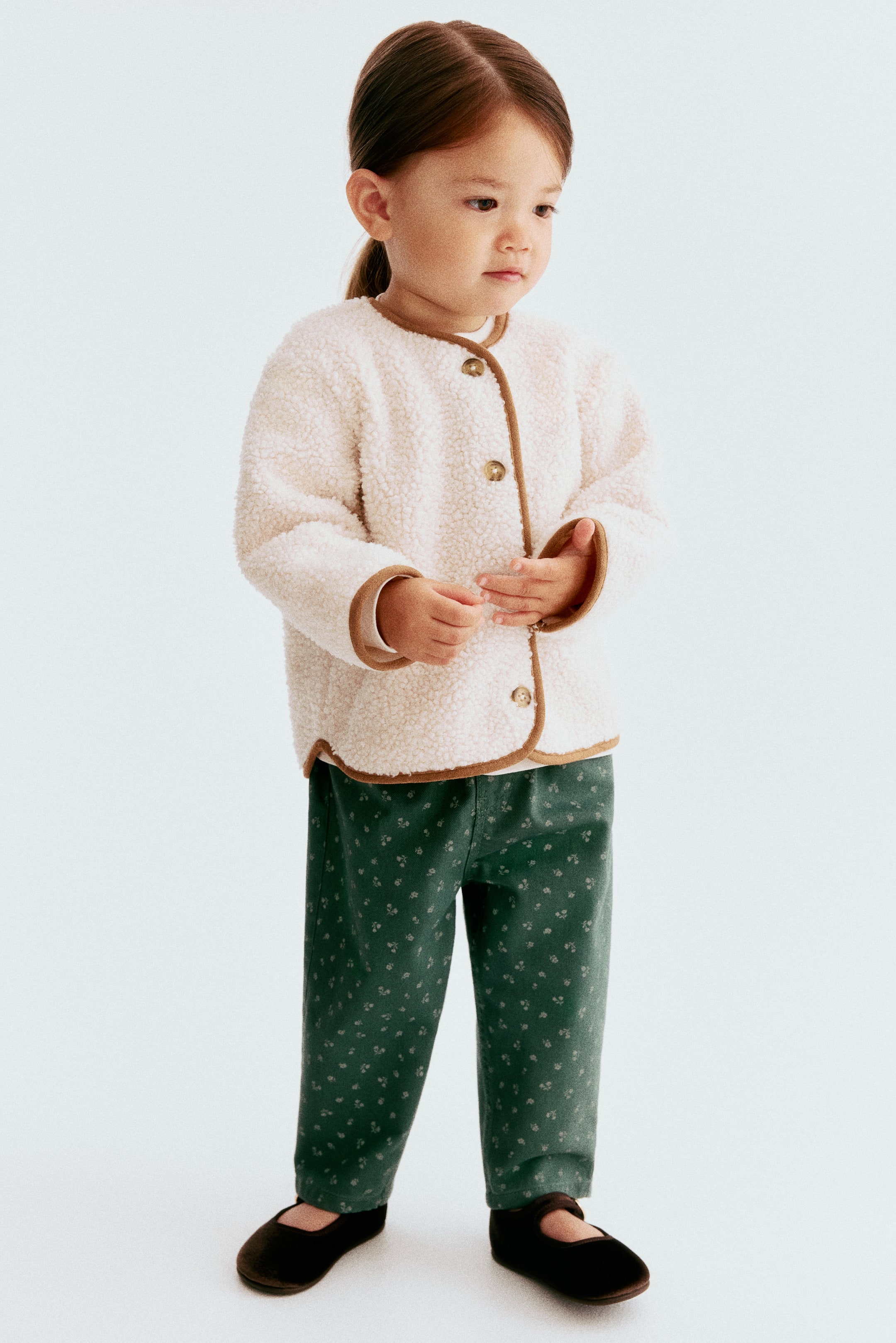 View larger image: Green trousers in a printed fabric are shown from the front. They feature a subtle allover pattern of small light motifs, tapered legs, and decorative front pockets.