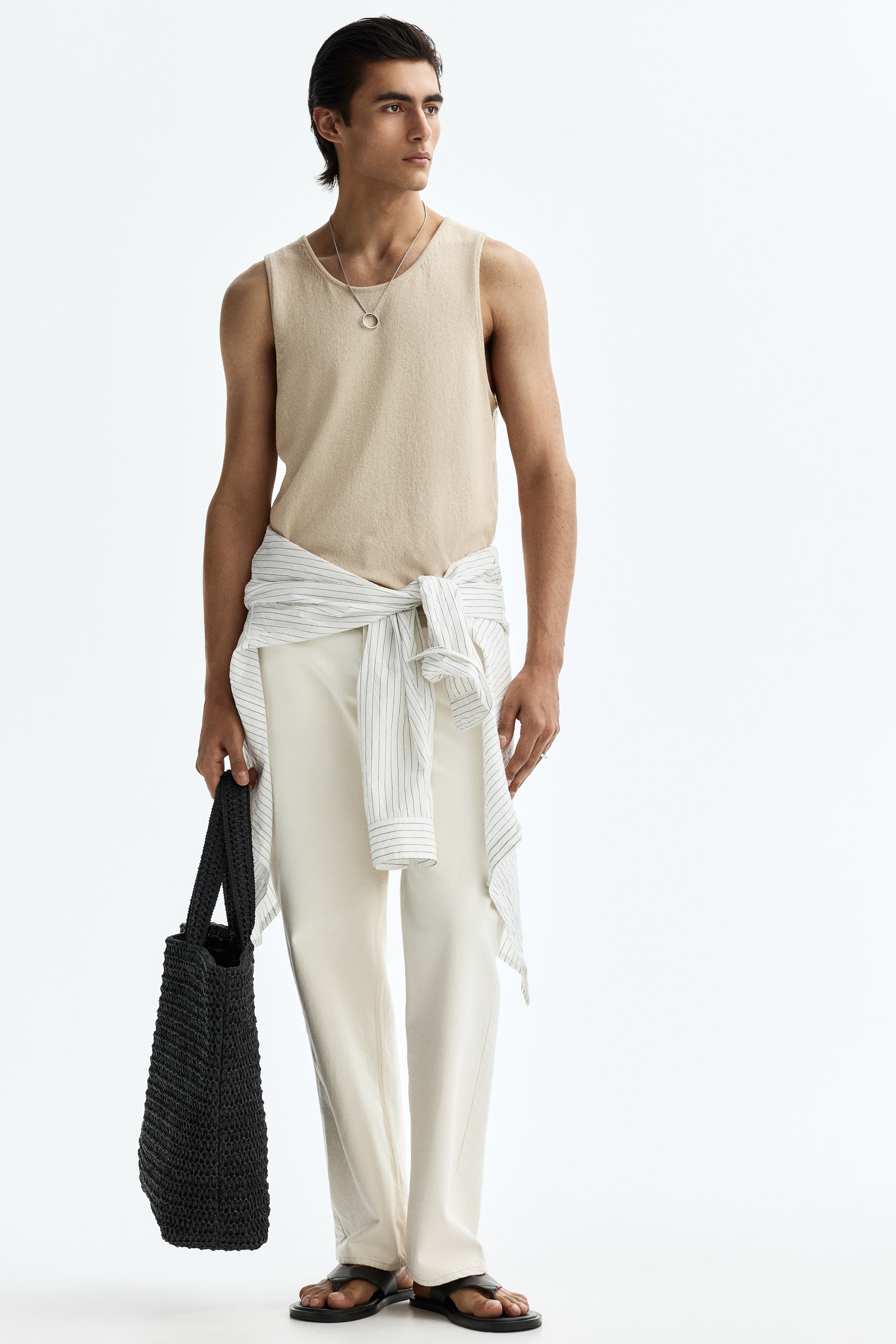 Ver imagen más grande: Pantalones anchos de color crema presentados desde un ángulo ligeramente frontal izquierdo, con un ajuste holgado y una sutil línea vertical a lo largo de cada pierna, con una camisa de rayas atada a la cintura y el dobladillo a la altura del tobillo descansando justo por encima de unas sandalias negras.