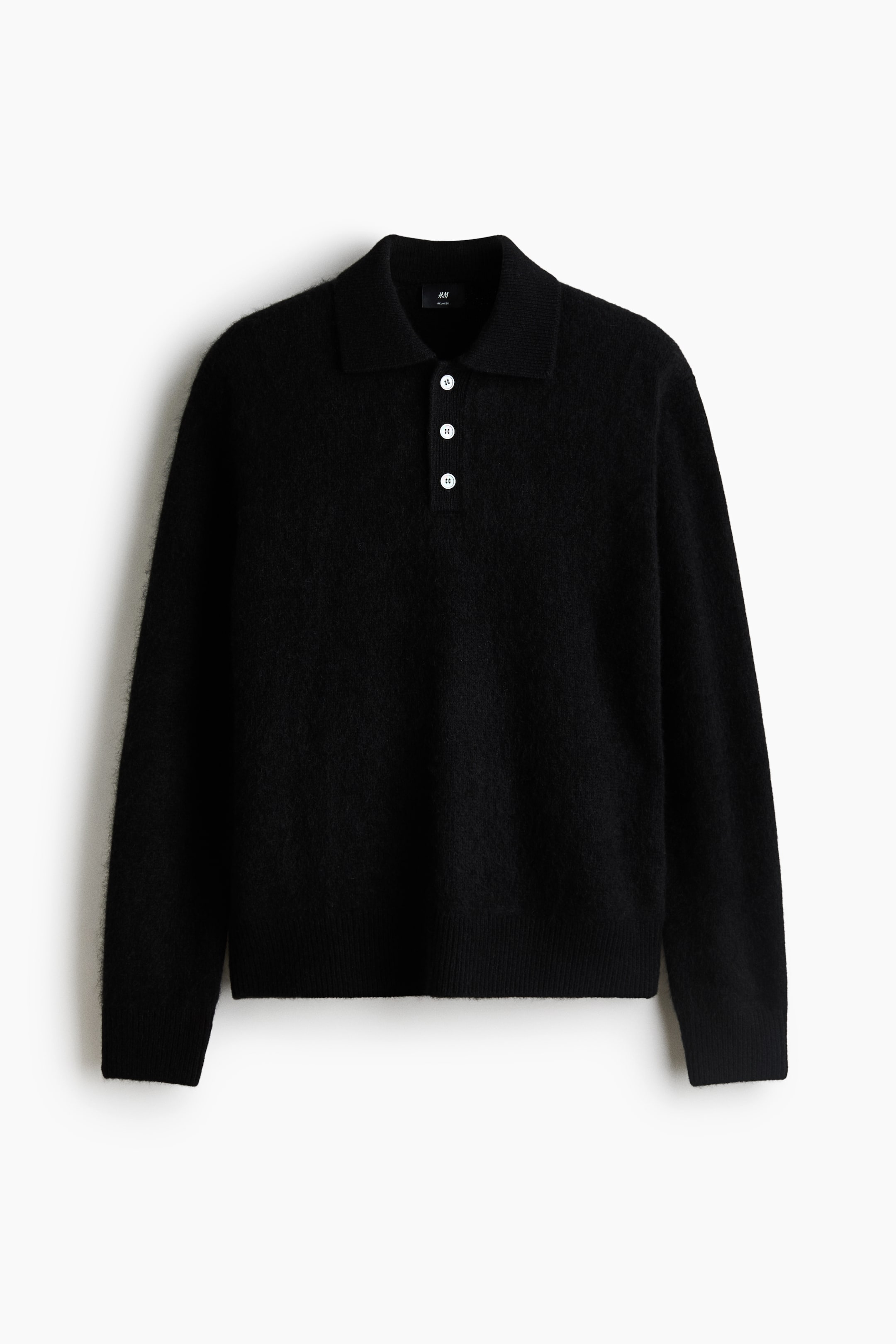 Agrandir l'image: Un polo noir à manches longues en maille de laine douce et duveteuse est présenté de face, mettant en valeur un col classique, une patte de boutonnage à trois boutons avec des boutons blancs contrastants, ainsi que des finitions côtelées aux poignets et à l’ourlet.