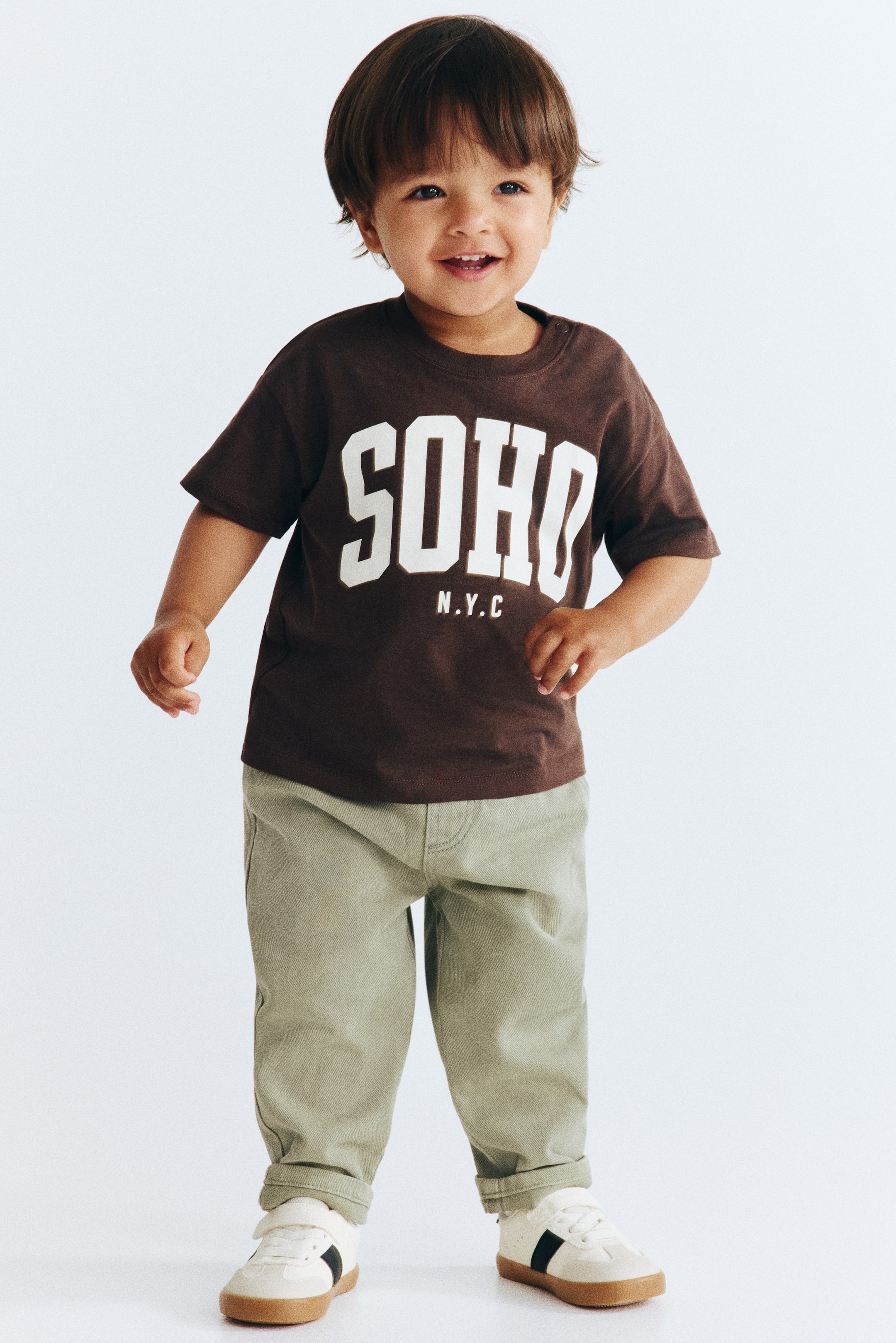 View larger image: Trousers in soft cotton twill are showing a front view, featuring an adjustable elasticated waist with a decorative drawstring and a fake fly. Decorative front pockets are detailing the front of the trousers.