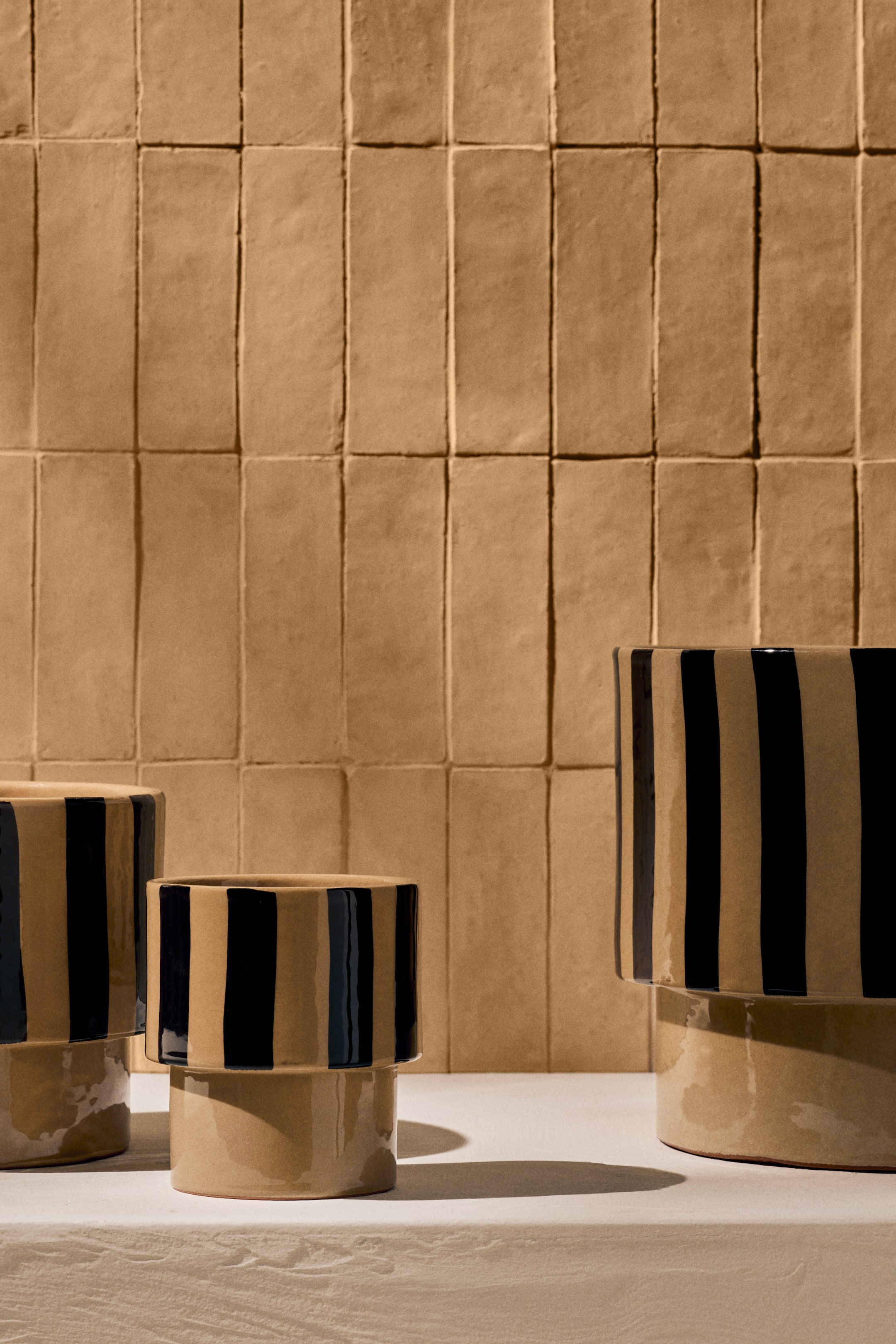 Ver imagem maior: Três vasos cilíndricos de cerâmica apresentam um design de dois níveis, com uma base bege e uma secção superior pintada com riscas verticais pretas irregulares; variam em altura e largura.