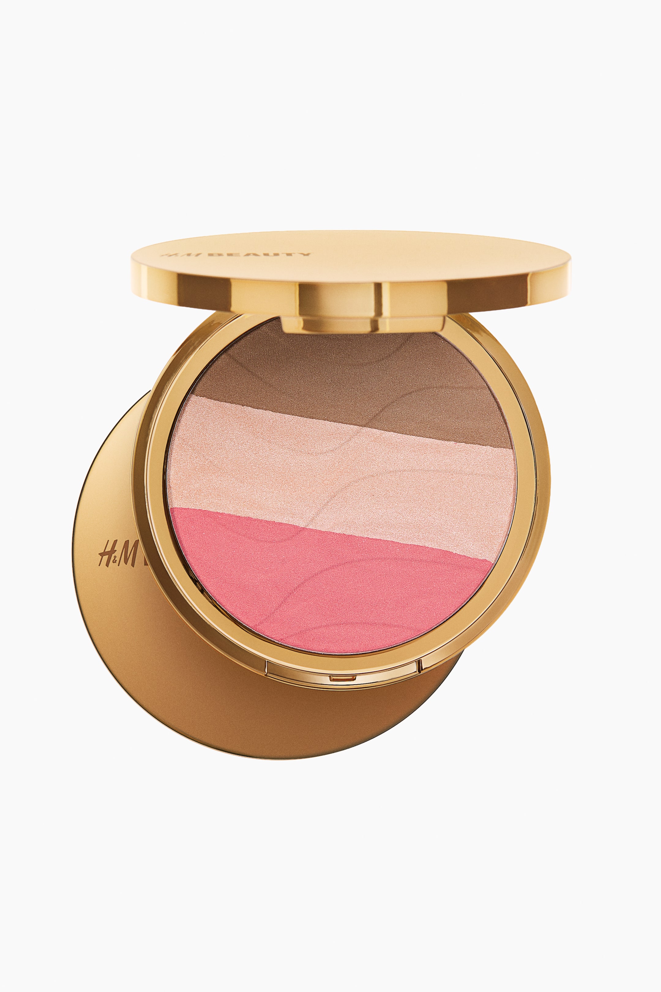 View larger image: A circular, gold-toned 3-in-1 pressed powder face palette is shown open, revealing a brown bronzer, a shimmery light pink highlighter, and a coral pink blush arranged in three horizontal strips, all with a subtle wave pattern. The open lid displays "H&M BEAUTY", and the base is embossed with "H&M".