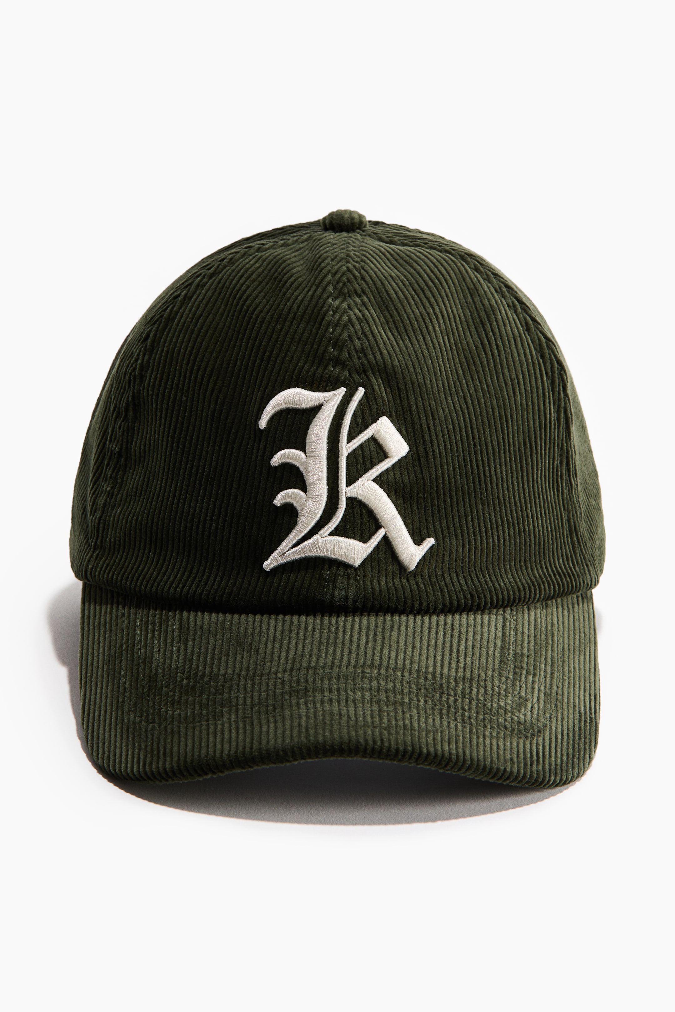 View larger image: A dark green corduroy cap features a white embroidered stylized "R" motif prominently displayed on the front of the crown.
