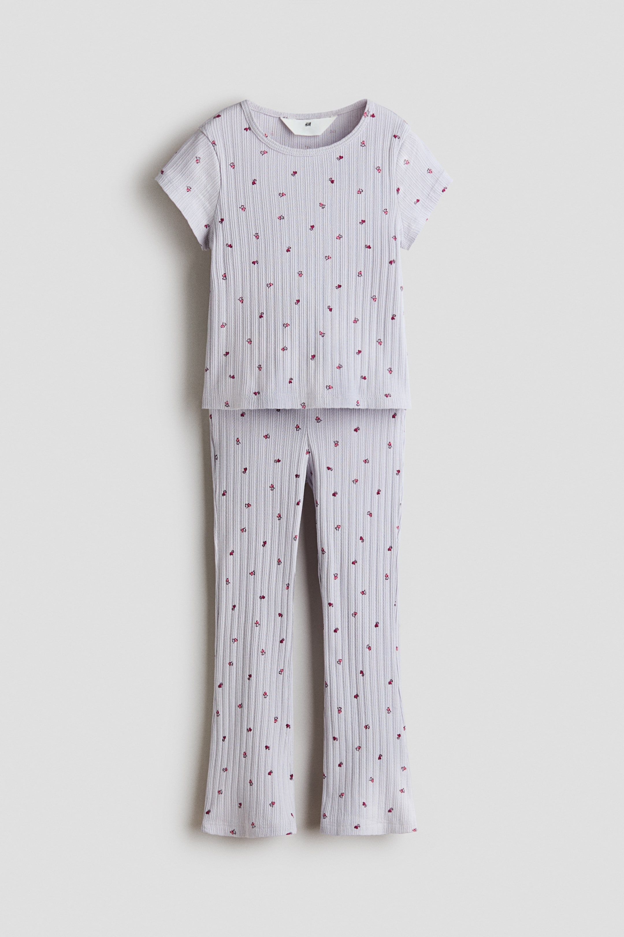 Ver imagen más grande: Conjunto de dos piezas de color lila claro acanalado, compuesto por un top de manga corta con cuello redondeado y pantalones largos con un ligero vuelo. Ambas piezas están decoradas con pequeños motivos rojos.