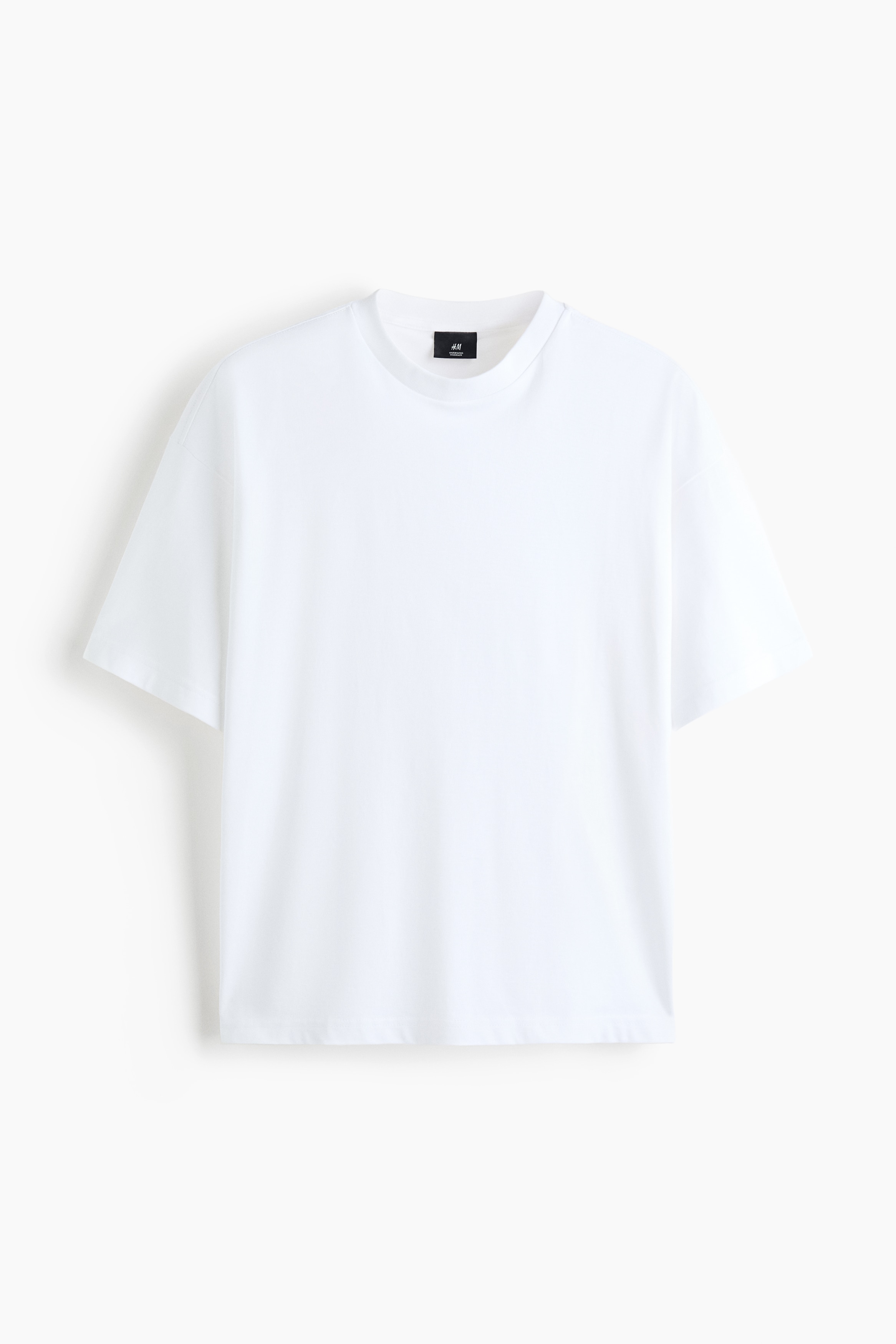 Una t-shirt bianca oversize presenta un girocollo a coste e maniche corte e ampie con spalle cadenti. Mostra una vestibilità rilassata e un orlo dritto visto da un'angolazione frontale.