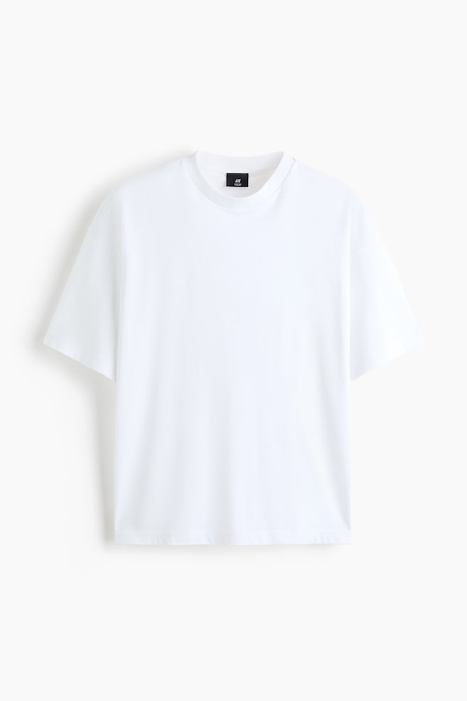 A front-facing view of a white boxy-style T-shirt in cotton jersey, featuring an oversized fit with dropped shoulders and wide, short sleeves. The T-shirt shows a round, rib-trimmed neckline and a straight-cut hem, highlighting its loose, baggy silhouette. - 1