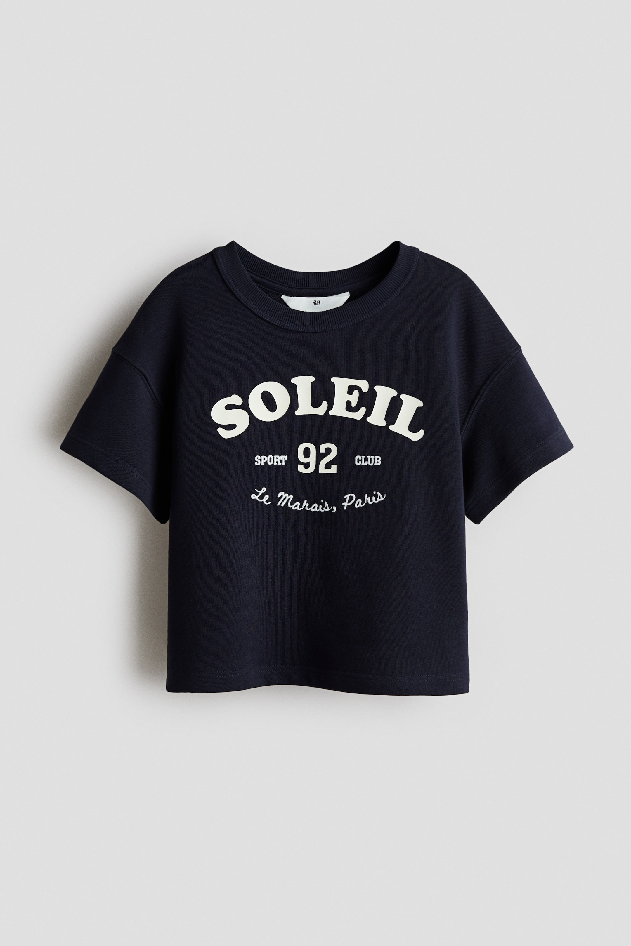 View larger image: A dark blue, boxy-style T-shirt is presenting its FRONT, featuring a lightweight sweatshirt fabric, a rib-trimmed crew neckline, and dropped shoulders. A white graphic print is appearing on the front, reading "SOLEIL" in large letters, with "SPORT 92 CLUB" and "Le Marais, Paris" printed below it.