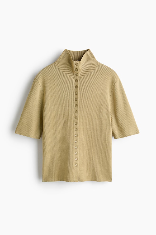 A tan ribbed knit top is featuring a high mock neck and short sleeves. A full button placket with small, round, matching-colored buttons is running down the center front. - 1