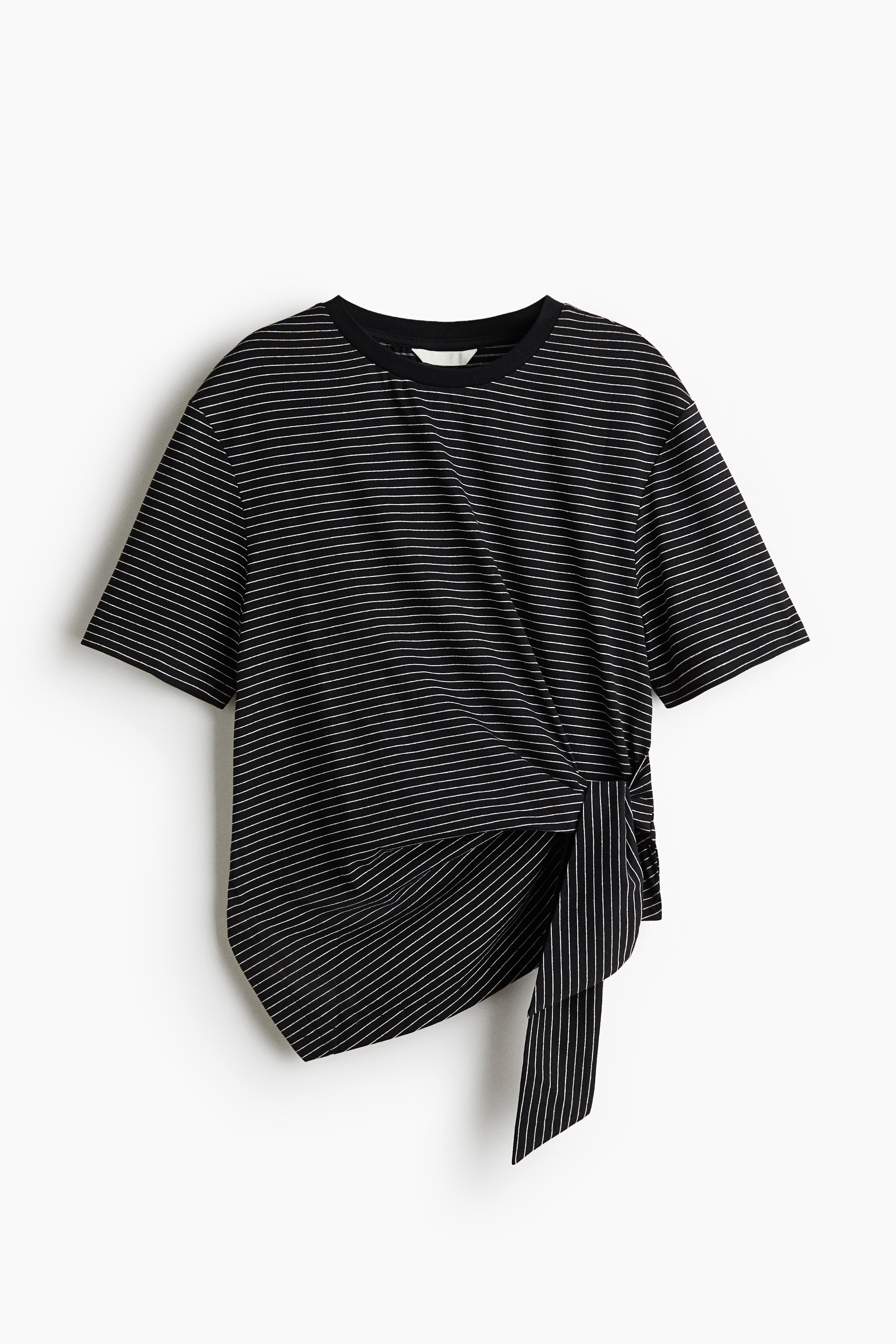 The model is wearing a black and white finely striped jersey top, featuring a round neckline, short sleeves, and an asymmetrical front hem tied on one side. The top is styled with dark blue denim jeans.