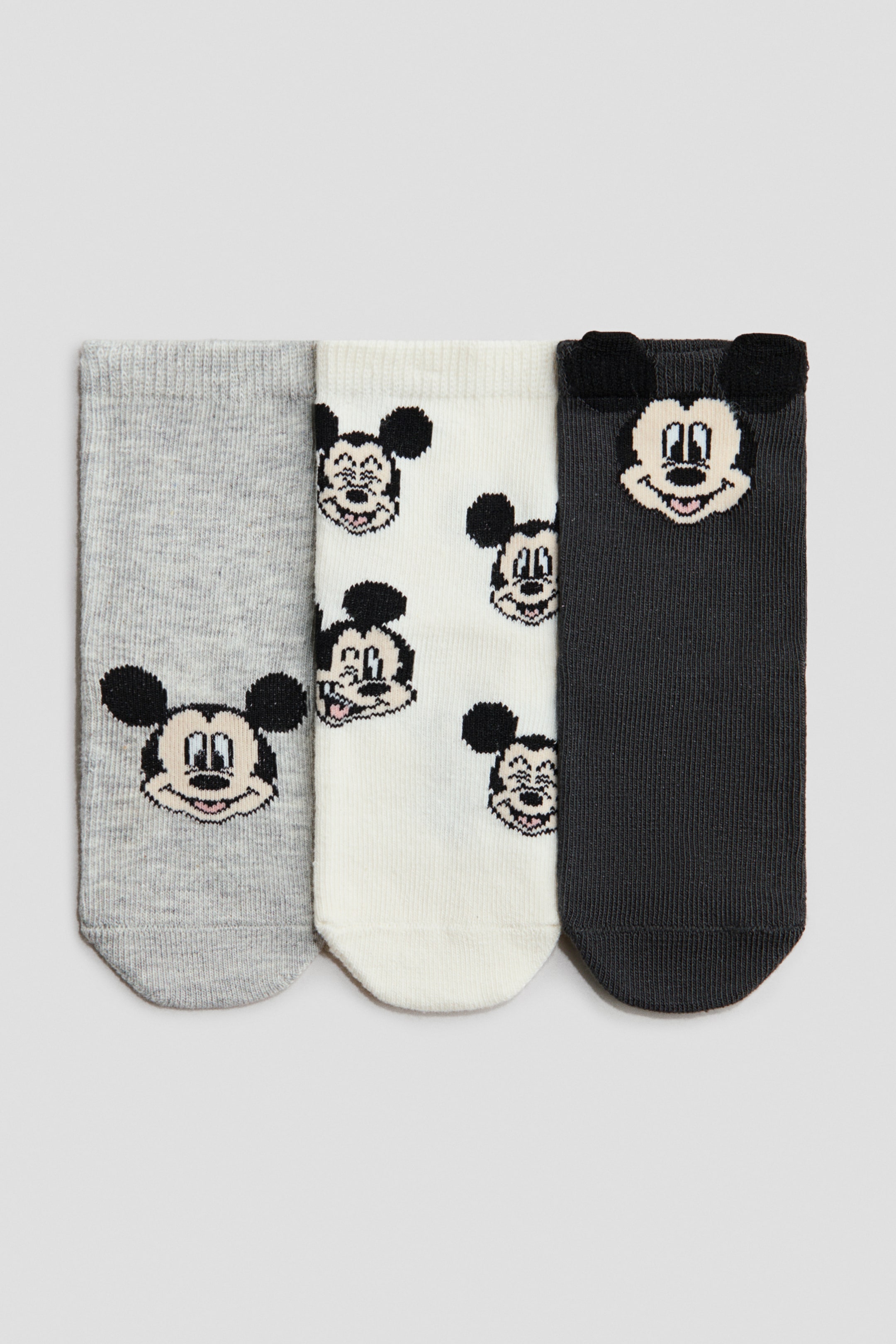 View larger image: Three pairs of fine-knit socks are presenting their FRONT. The gray sock is featuring a single Mickey Mouse face, the white sock is displaying multiple Mickey Mouse faces, and the dark gray sock is showcasing a Mickey Mouse face with dimensional ears at its elasticated top.