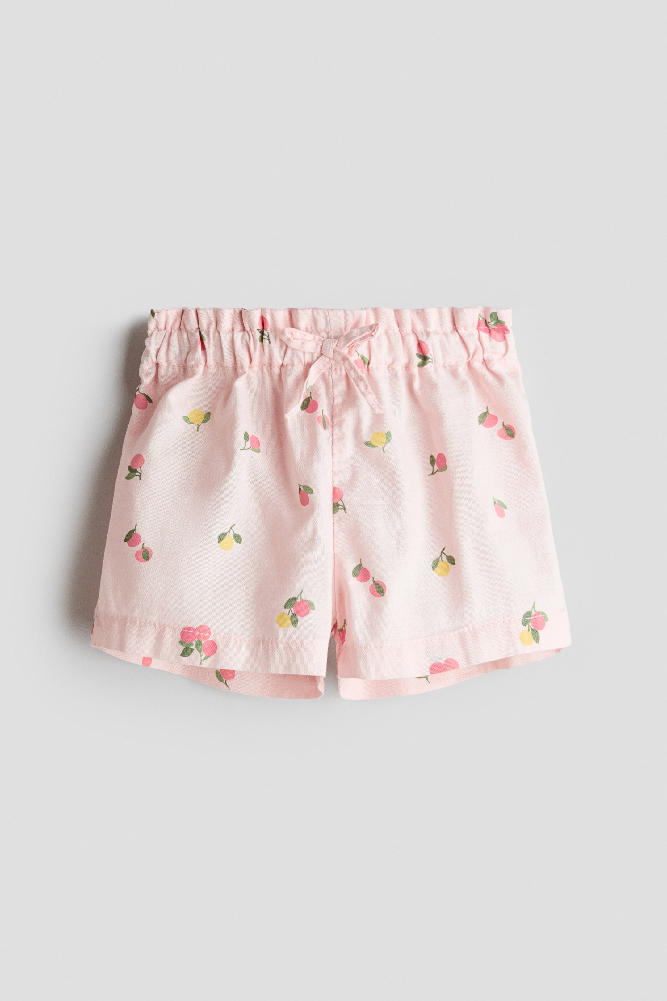 Größeres Bild ansehen: Die pinkfarbenen Shorts präsentieren ein weiches Gewebe mit einem sich wiederholenden Muster aus gelben und pinkfarbenen Früchten. Sie verfügen über einen verstellbaren Paperbag-Bund mit einer dekorativen Schleife, die vorne gebunden ist.