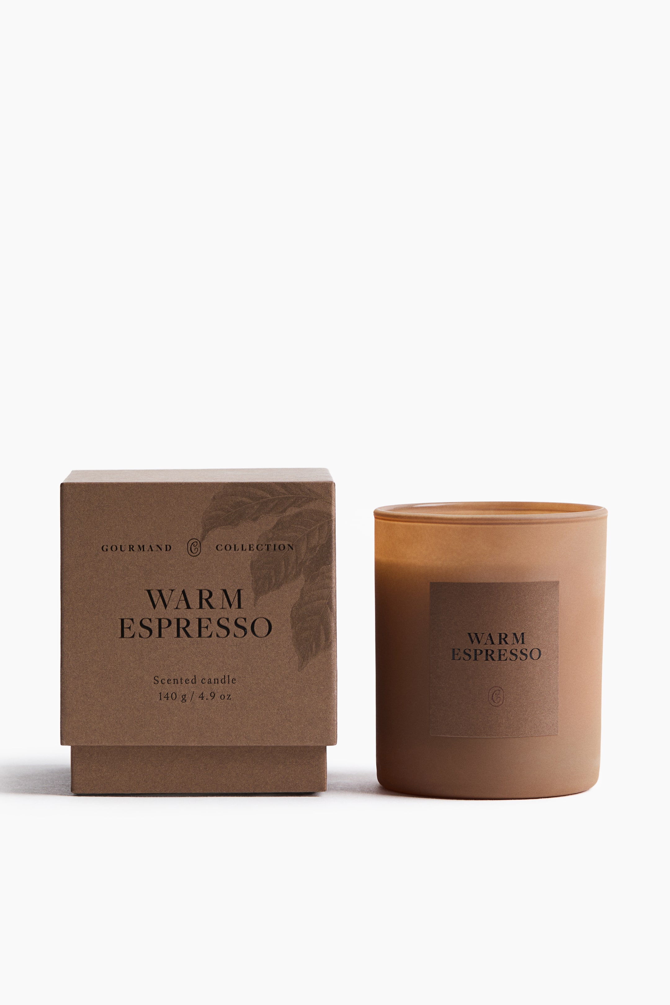 View larger image: A scented candle in a frosted amber-brown glass holder is placed next to its matching brown cardboard gift box, both facing forward. The candle holder and the two-piece box feature minimalist labels with the text "WARM ESPRESSO" printed in a clean black font.