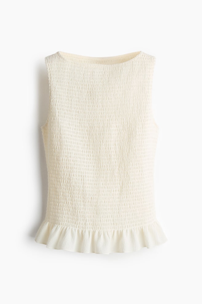 A cream sleeveless top is shown from the front. The top features a shirred texture across the body, a wide, rounded neckline and a ruffled hem. - 1